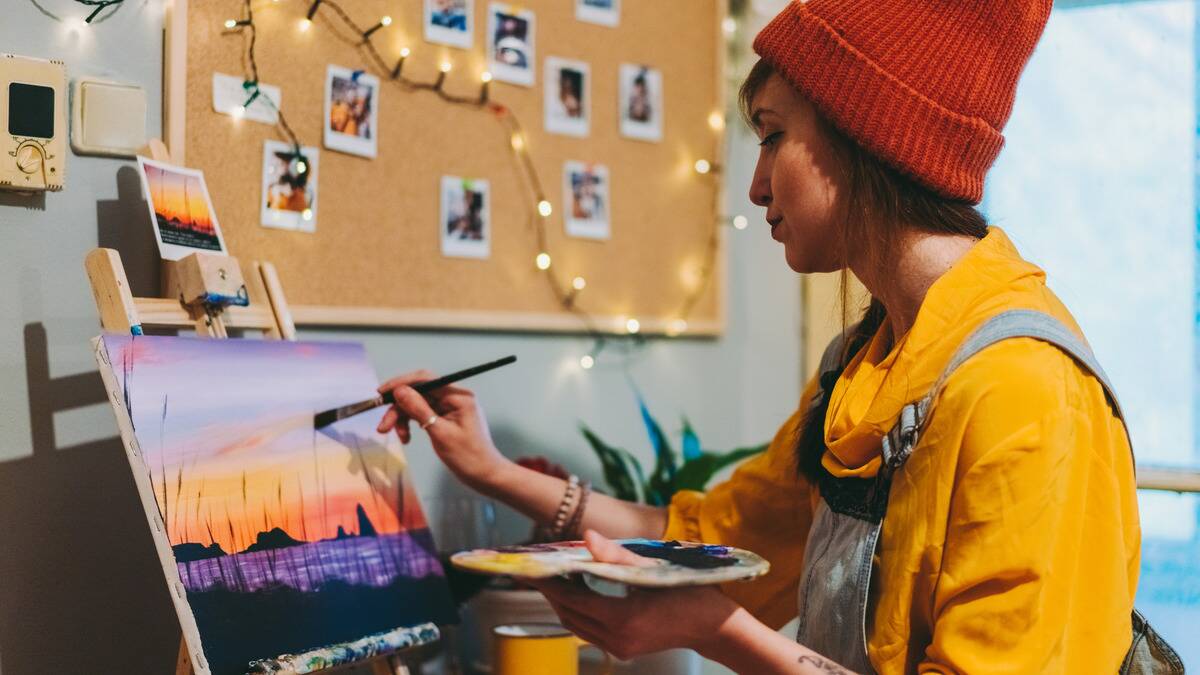 A woman sitting in her room, painting a landscape scene on an easle.