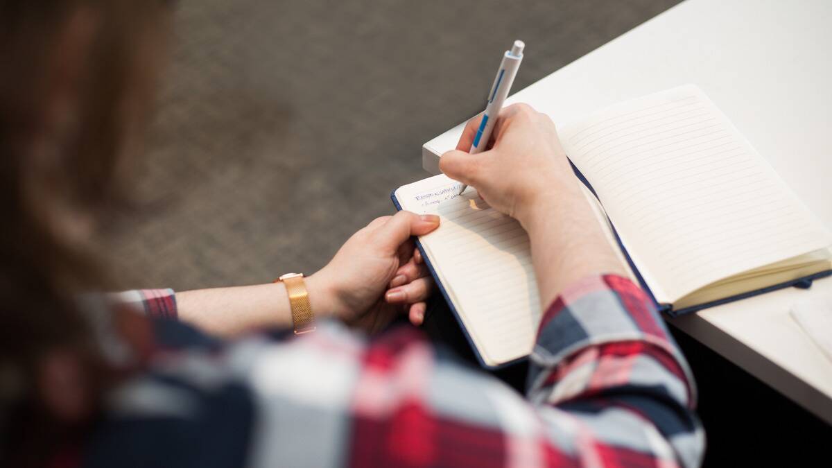 An over the shoulder shot of someone writing in an open page of a notebook.