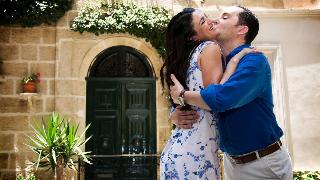 A couple embracing outside, the woman smiling as the man kisses her cheek.