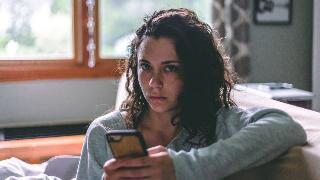 A woman looking up from her phone directly into the camera, sporting a serious look on her face.
