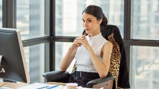 A woman, clearly a boss or manager of some kind, sat at her desk with her hands together, looking content and thoughtful.