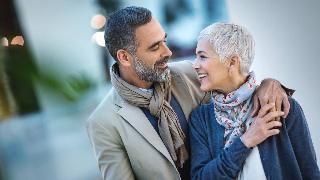 A couple standing outside, the man's arm around the woman, smiling at each other.