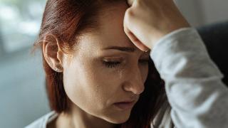 A closeup shot of a woman with a hand on her forehead, a tear on her cheek.