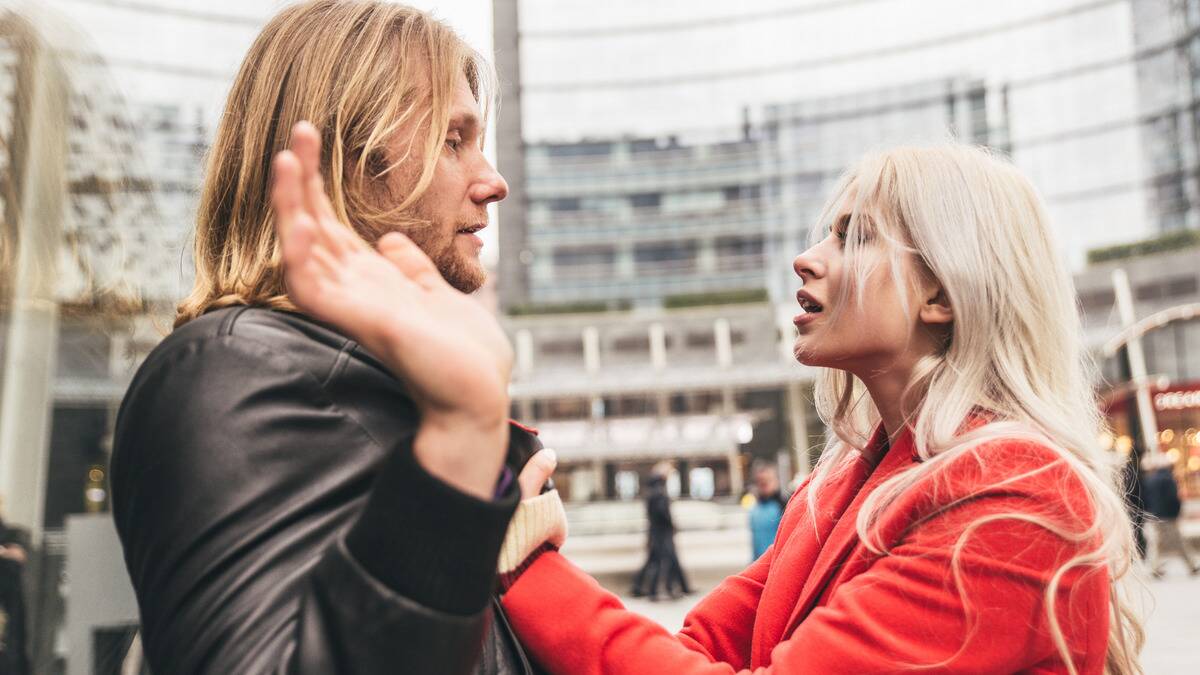 A couple fighting, the woman grabbing the man's jacket while he holds his hands up.