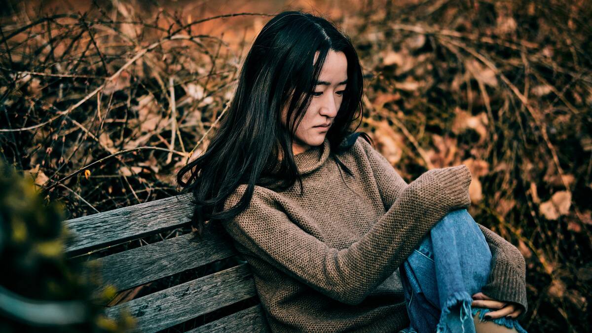 A woman sitting on a bench, looking down sadly.