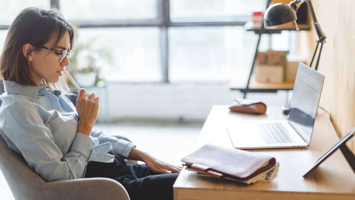 A woman sitting in her office chair, her pen up to her lips, in thought.