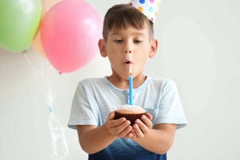 A kid holding a cupcake with a large lit candle on top, about to blow it out after making a birthday wish