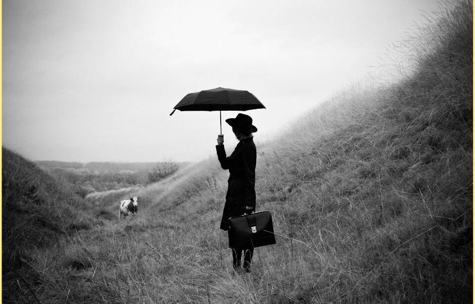 A woman standing in a valley holding an umbrella, in black & white