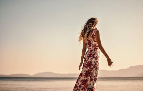 A woman in a dress standing on a beach, looking to the horizon