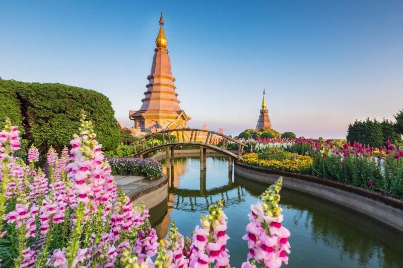An image from Thailand, showing beautiful flowers and architecture, as well as a bridege going over a serene river