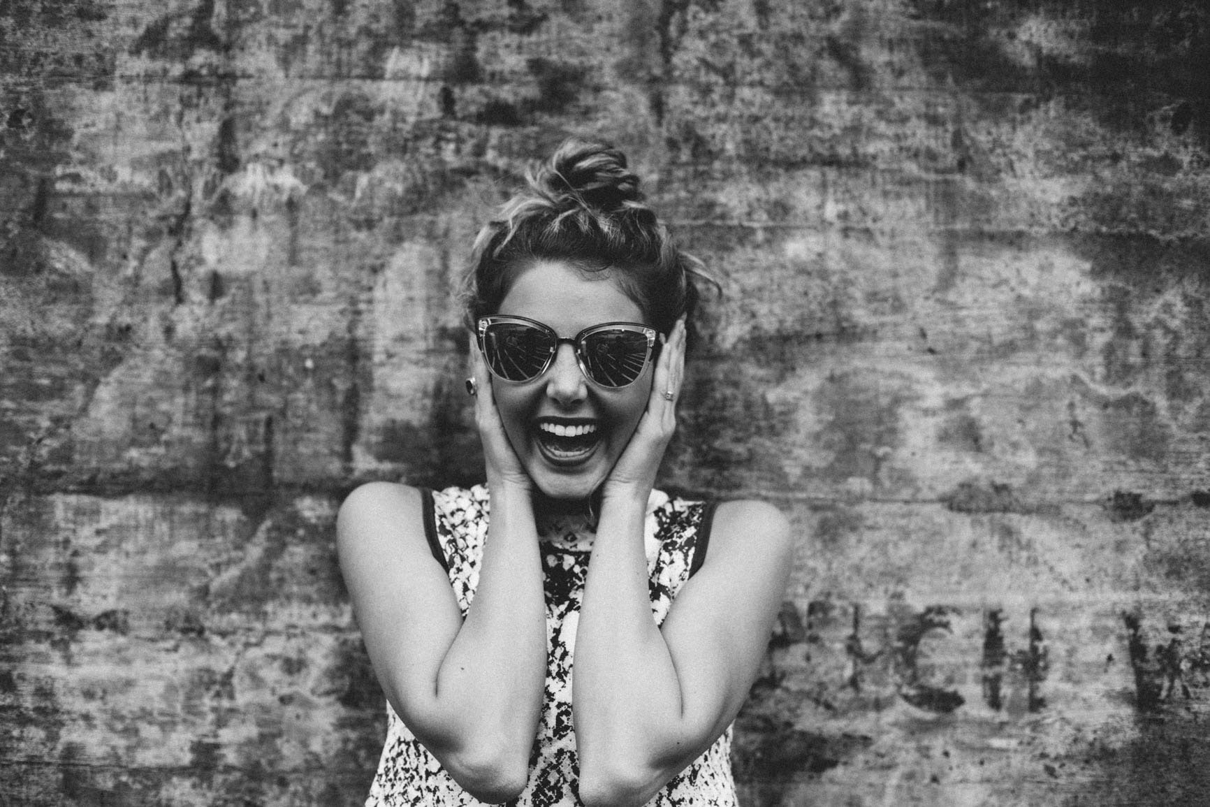 A greyscale image of a girl smiling, both hands on her face.