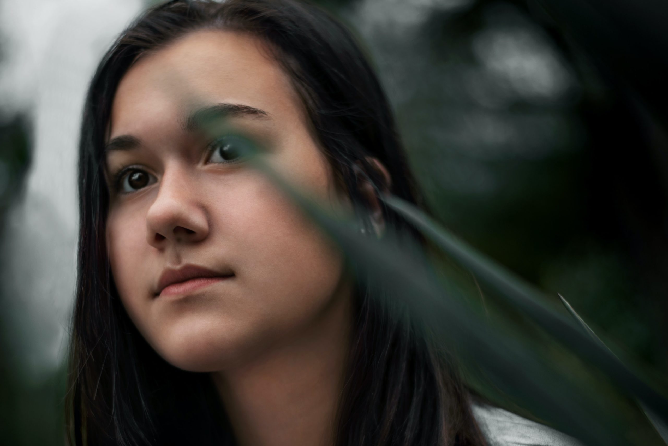 A woman looking forward seriously among some leaves.