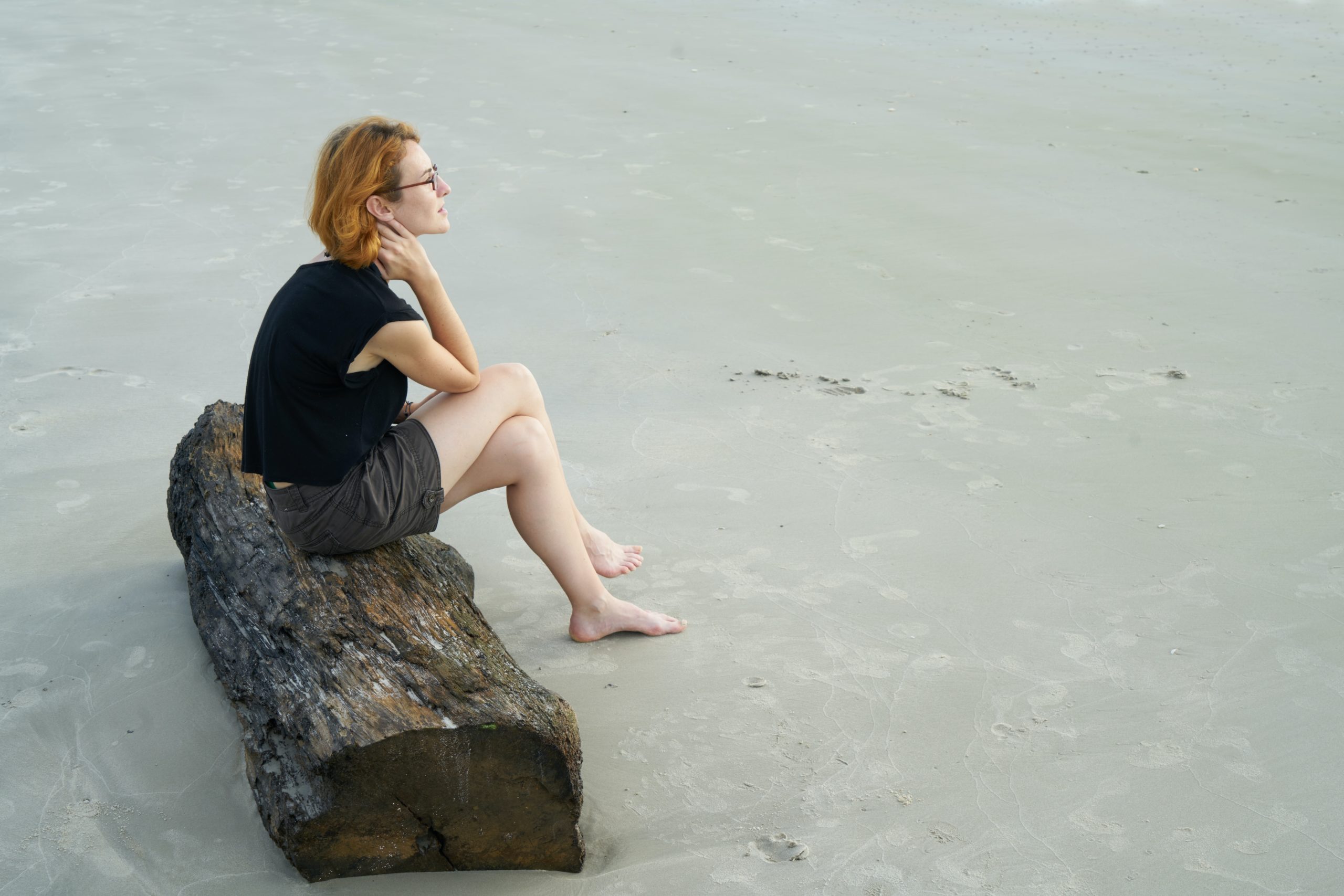 A woman sitting on a log on the beach.