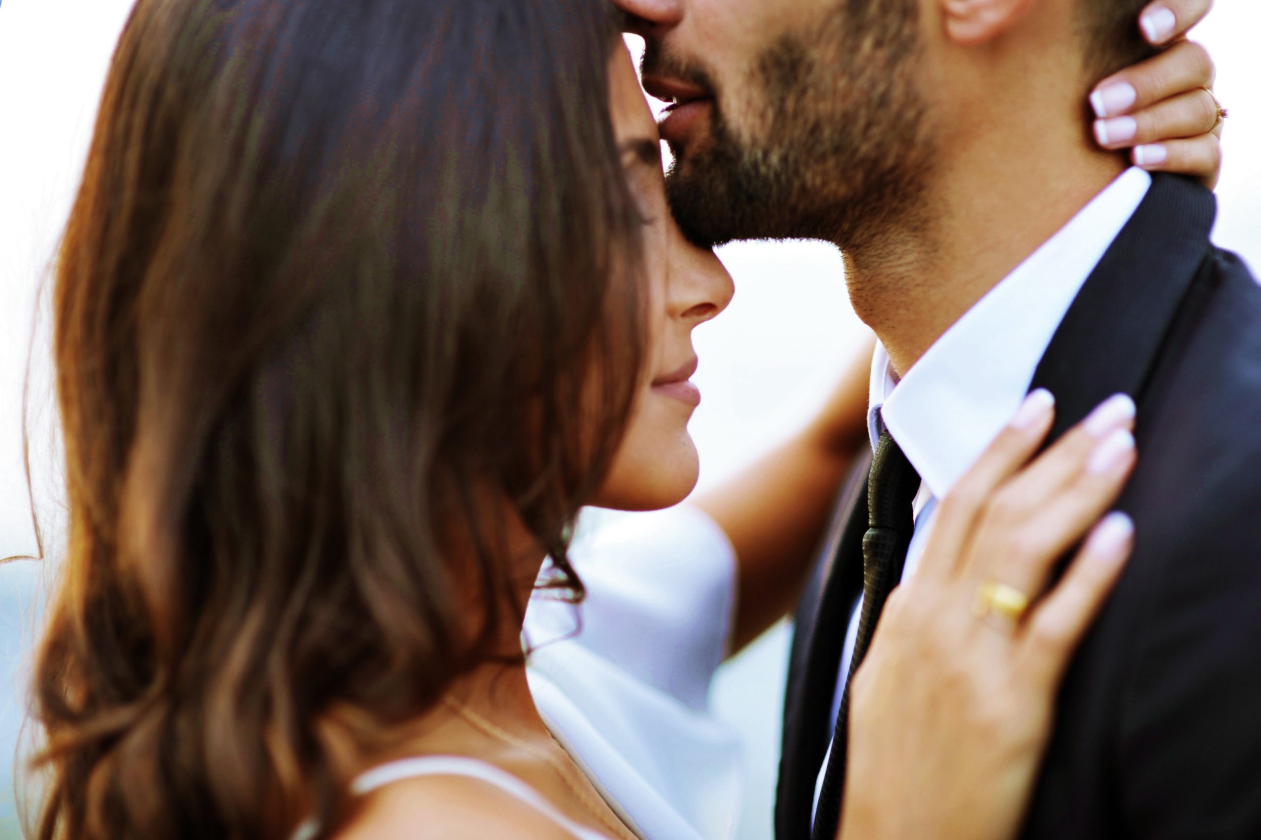 A closeup of a man kissing a woman's forehead as they embrace.