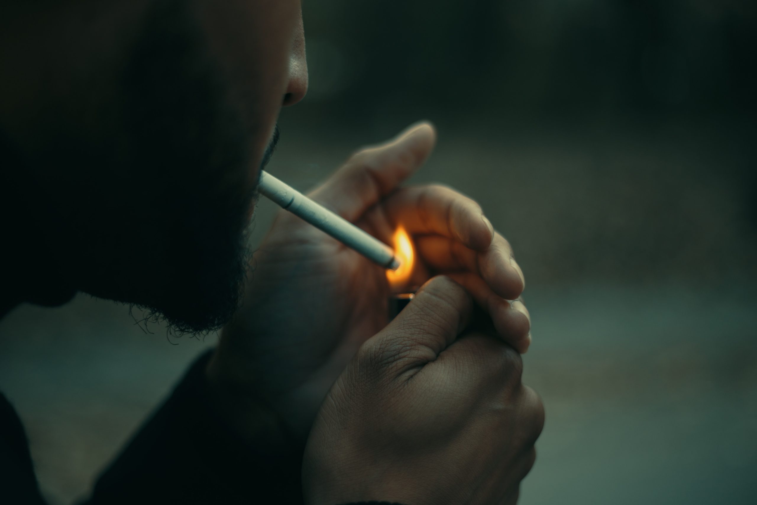 A man lighting a cigarette in his mouth.