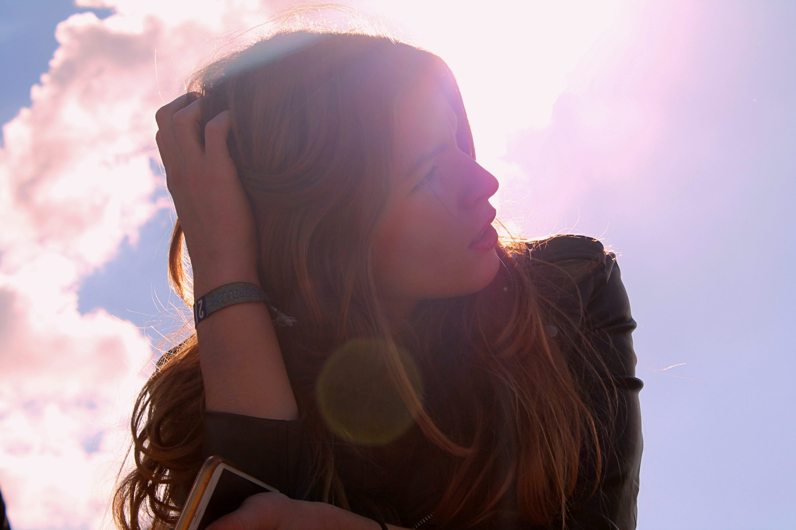 A woman with her hand in her hair, the sun shining behind her.
