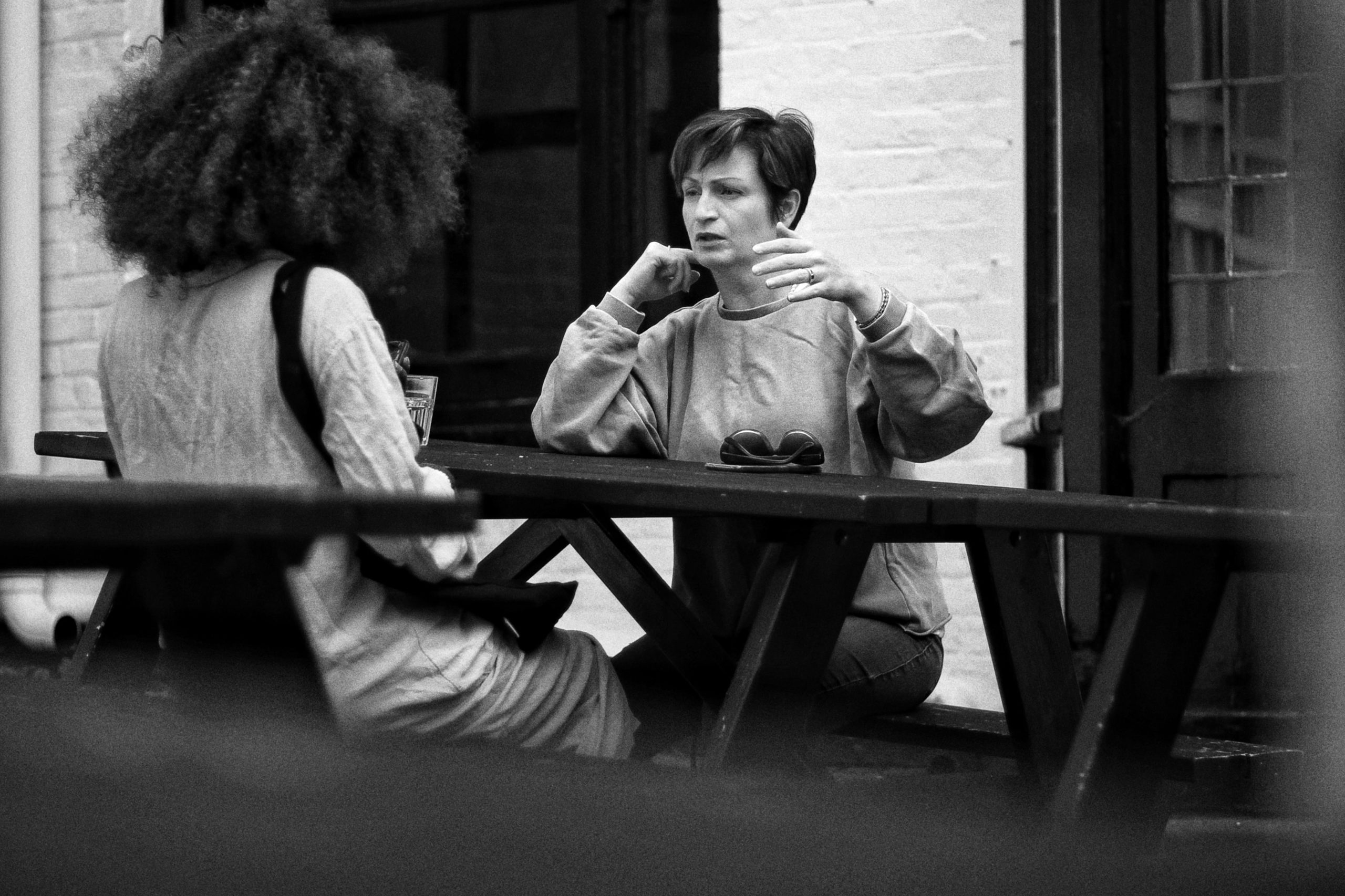 A greyscale image of two women sitting at a picnic table, talking.