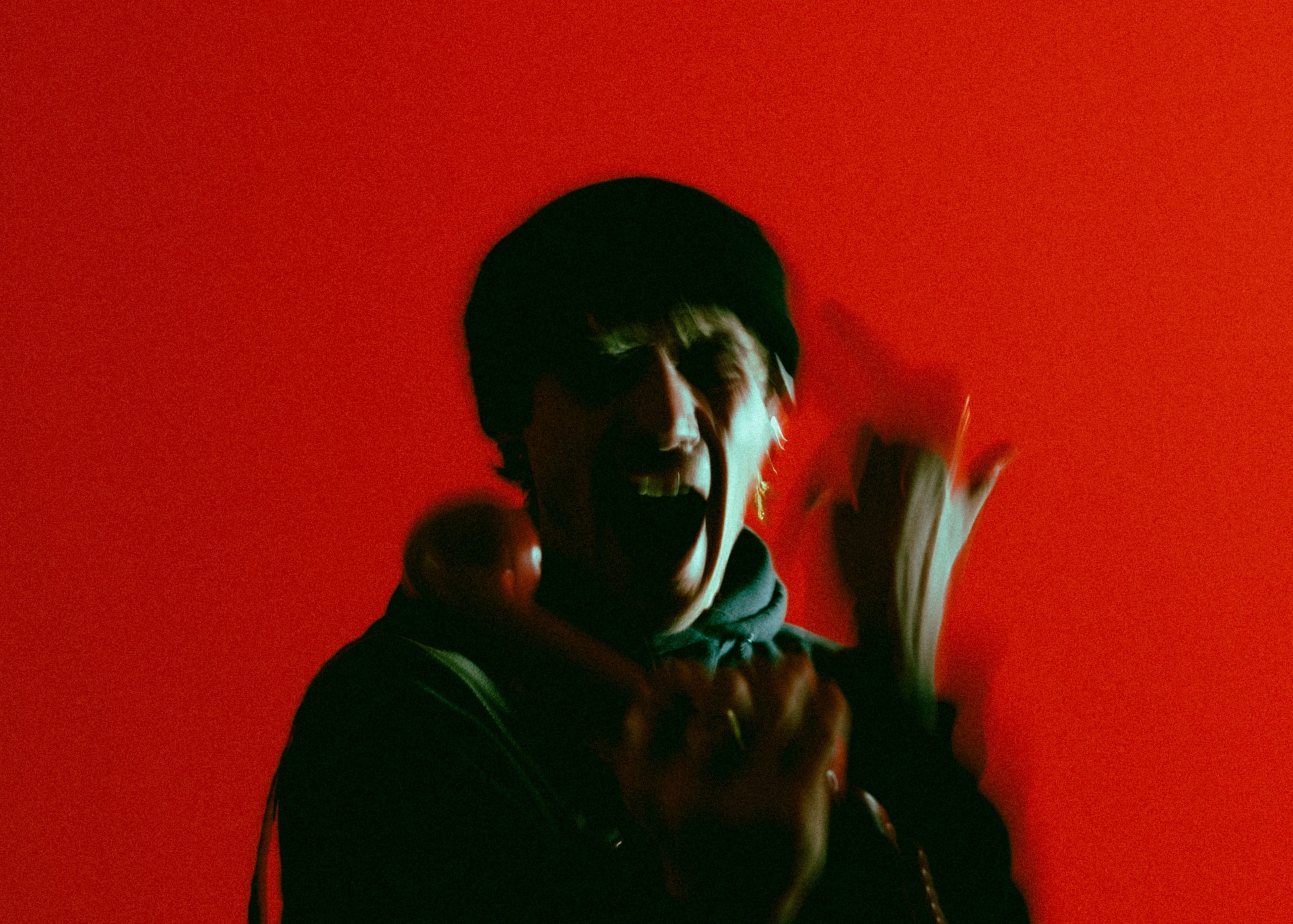 A blurry photo of a man yelling against a red background.