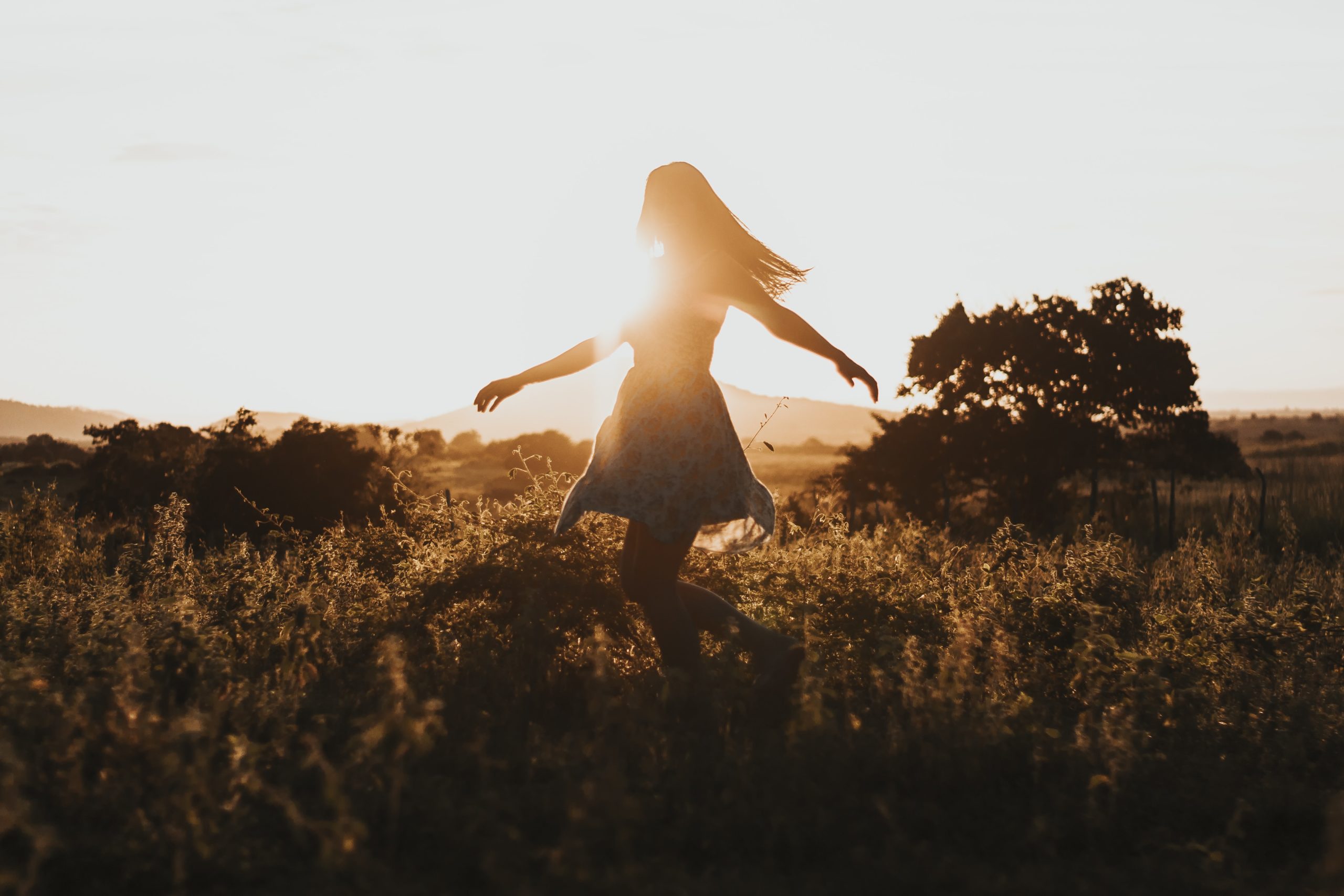 A silhouette of a woman spinning in a field of tall grass.