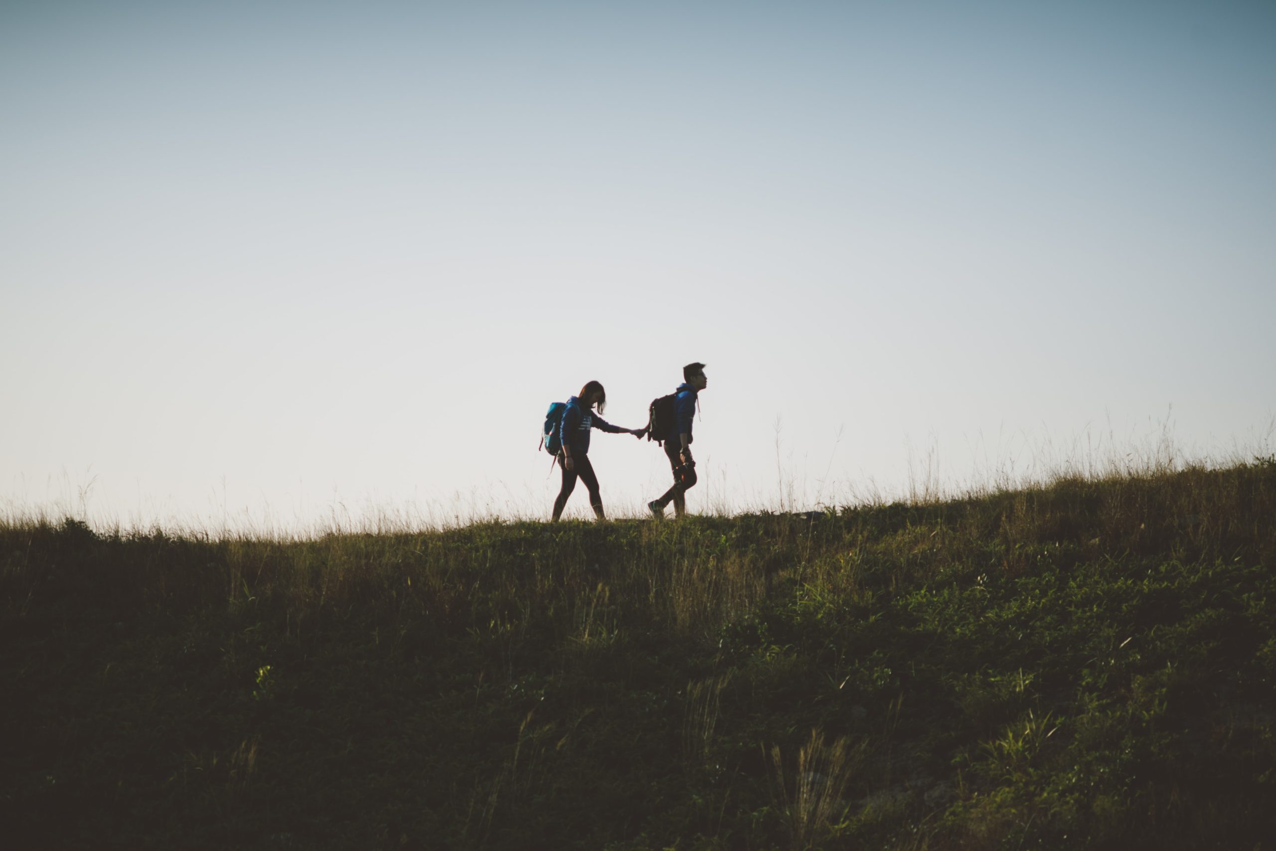 Two people walking along a hill range, holding hands.