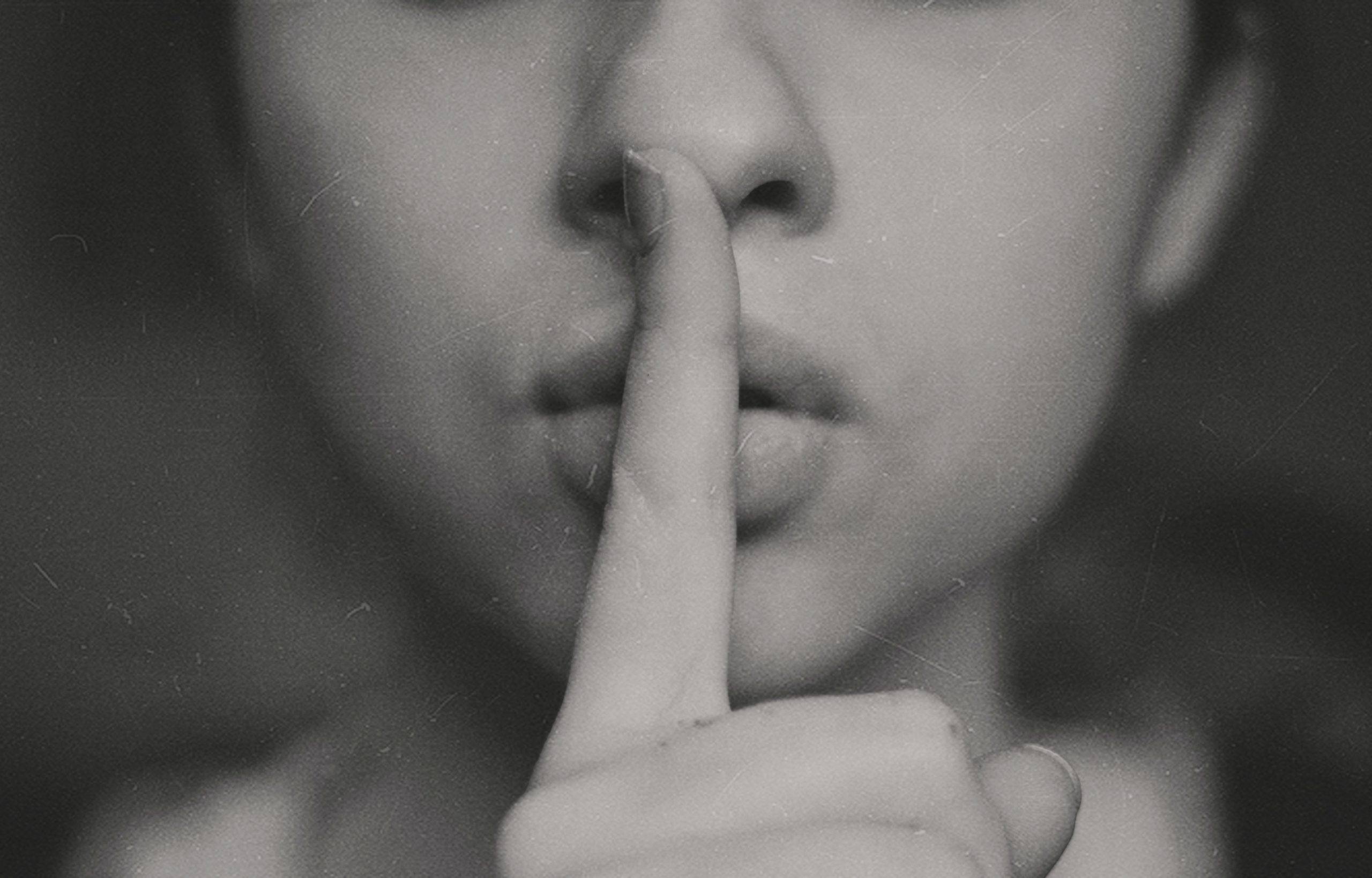 A greyscale image of a woman holding a finger to her lips.
