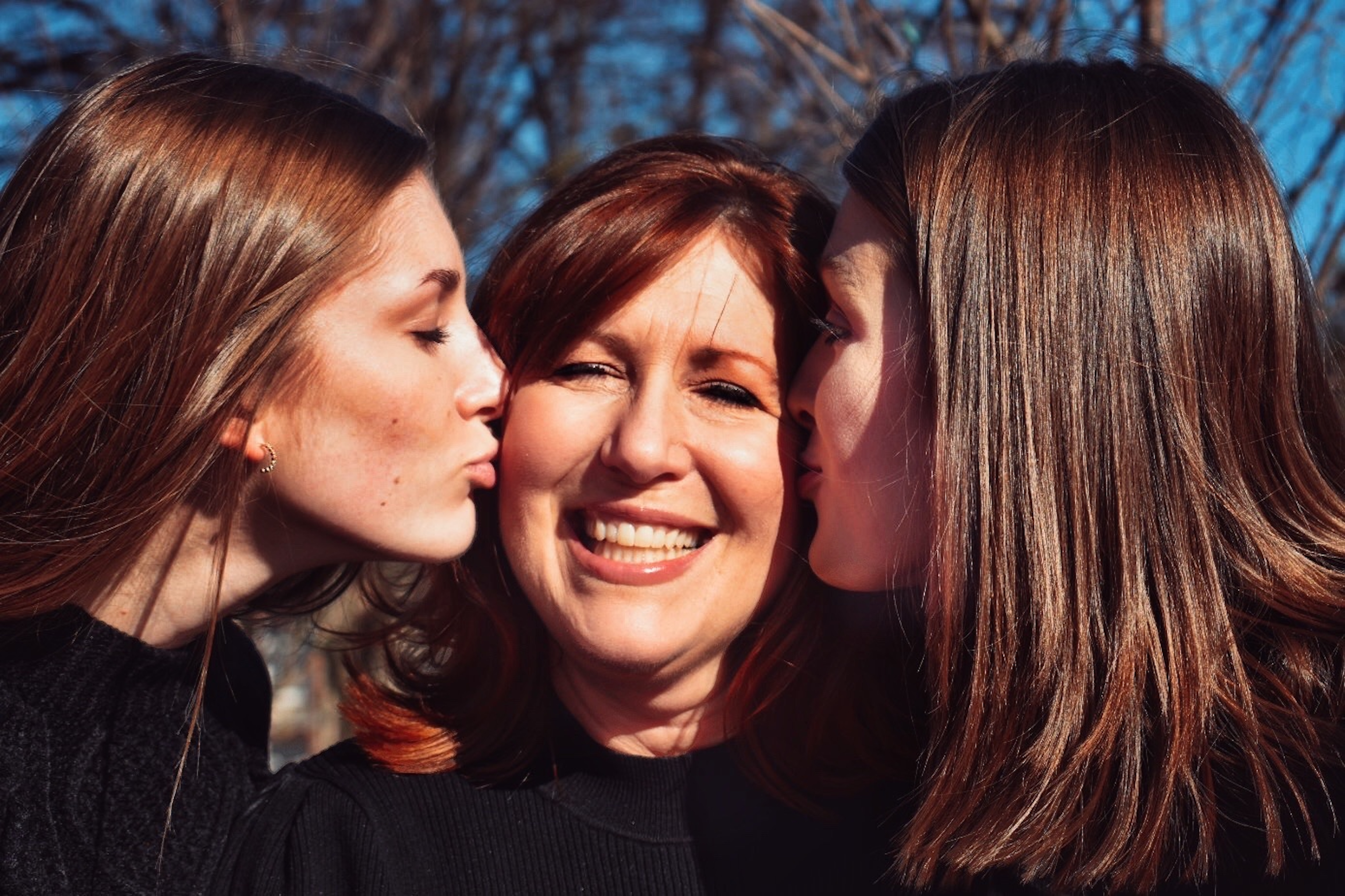 A mother being kissed on her cheeks by her two daughters.