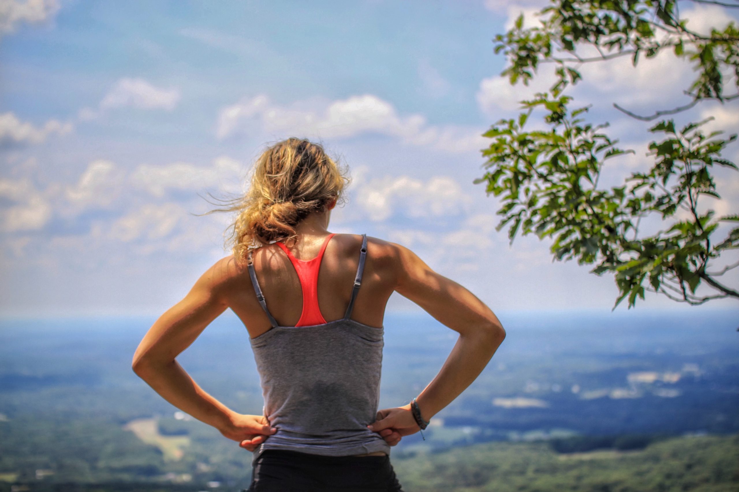 A fir woman in a tank top standing on a hill, looking outwards.