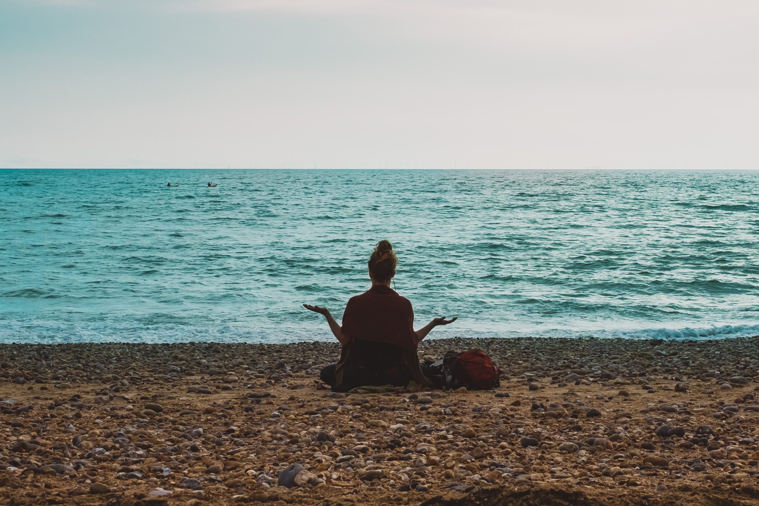 A woman sitting on a beach, meditating.