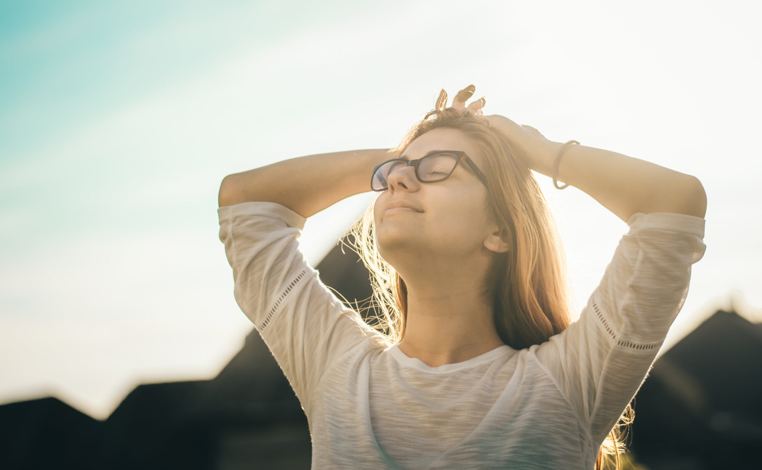 A woman smiling in the sun, looking up towards the sky.