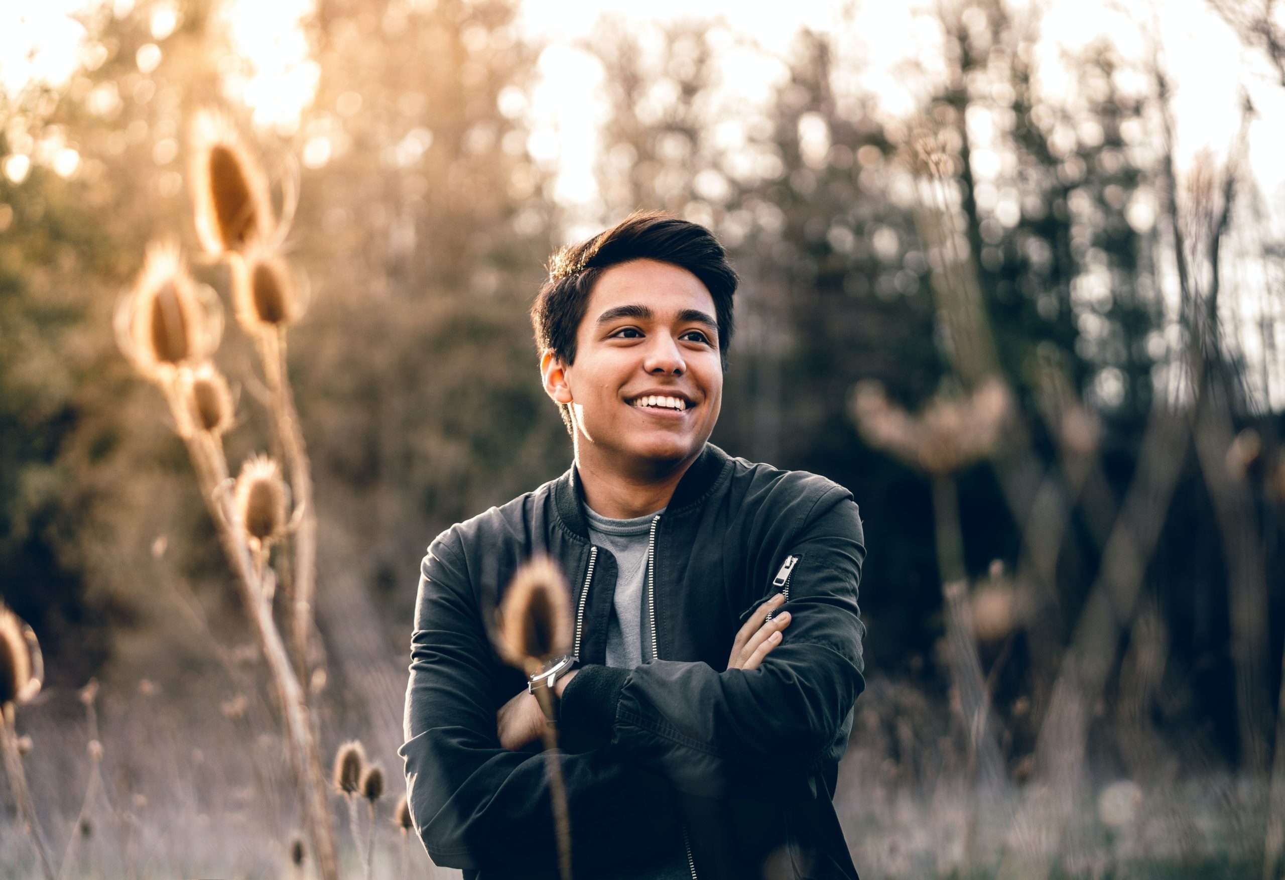 A young man smiling as he stands among some reeds.