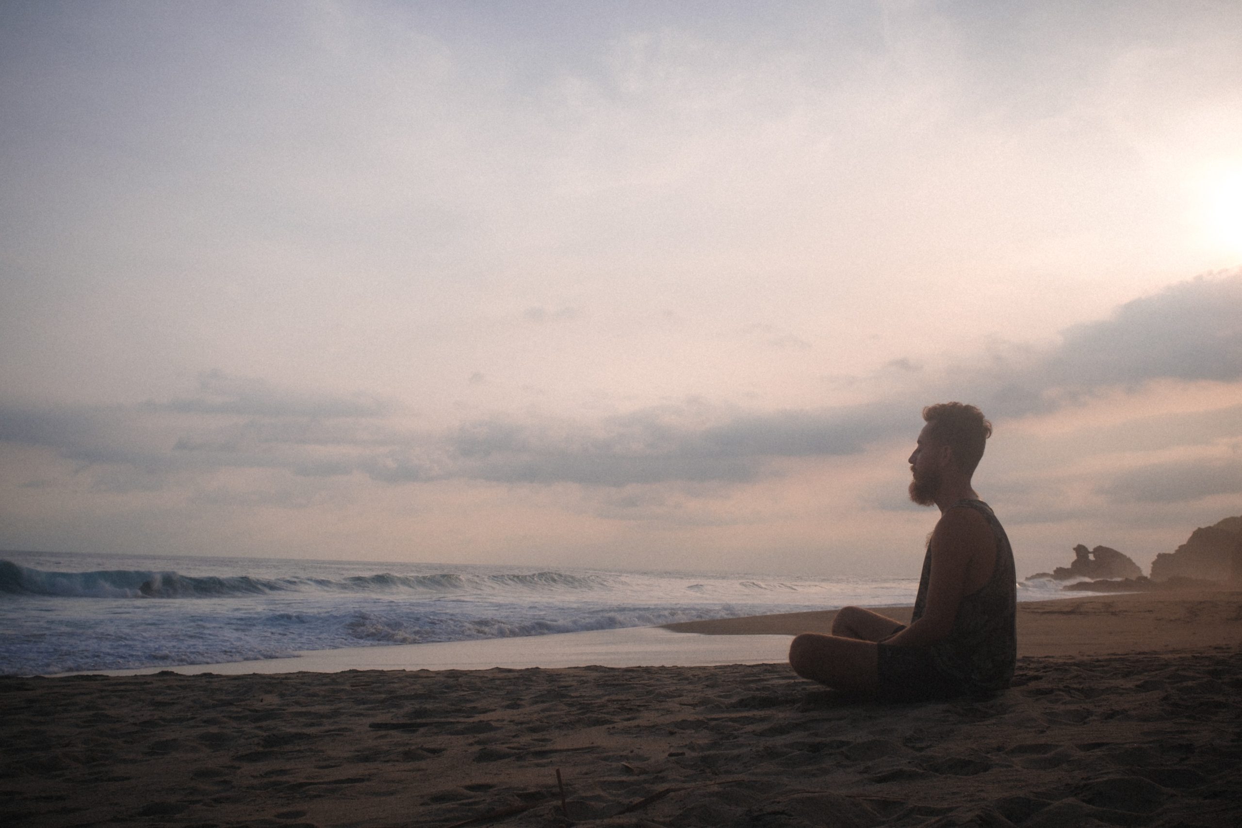 A man sitting on a beach meditating.