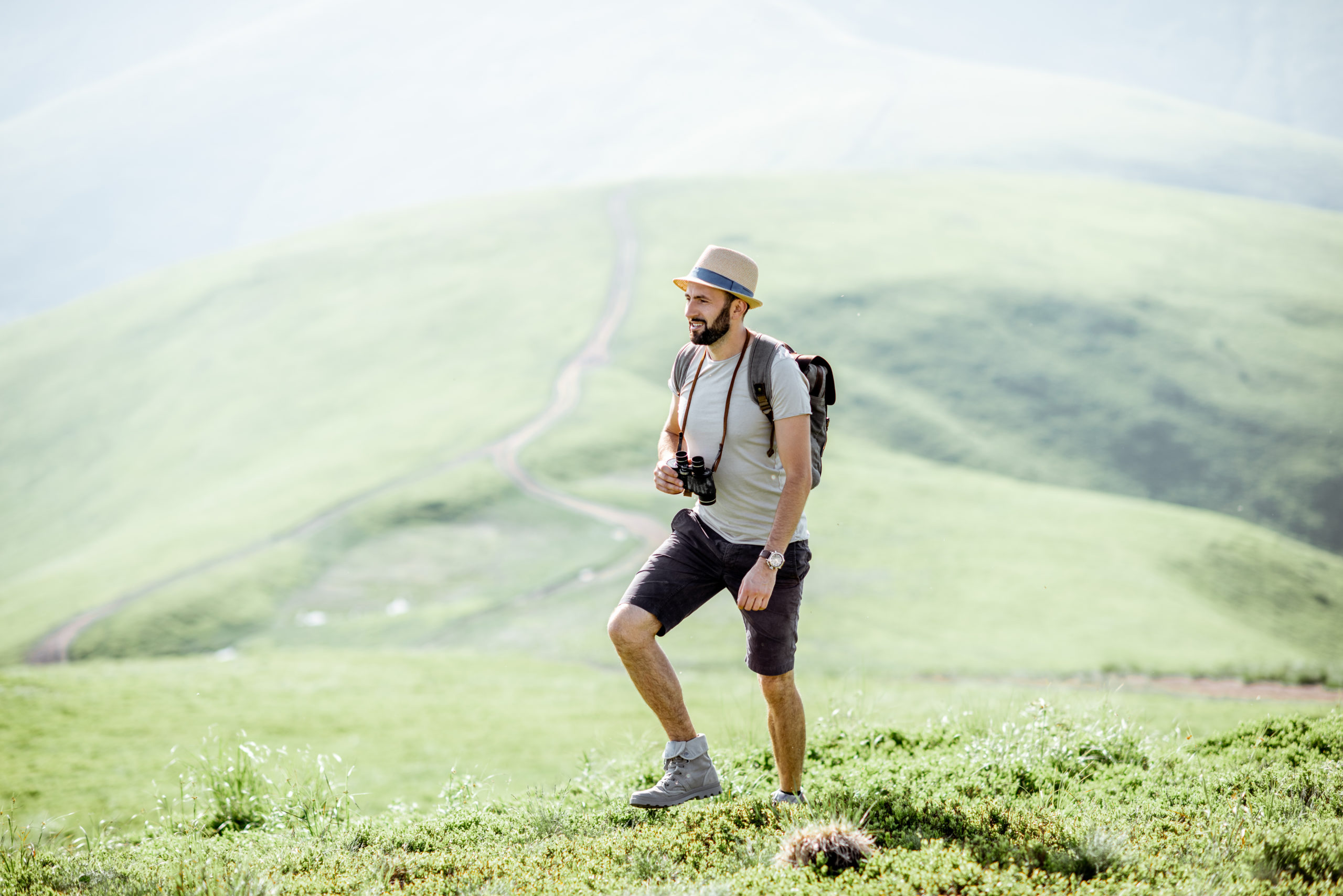 man with sun hat, camera, and backpack hiking through mountains