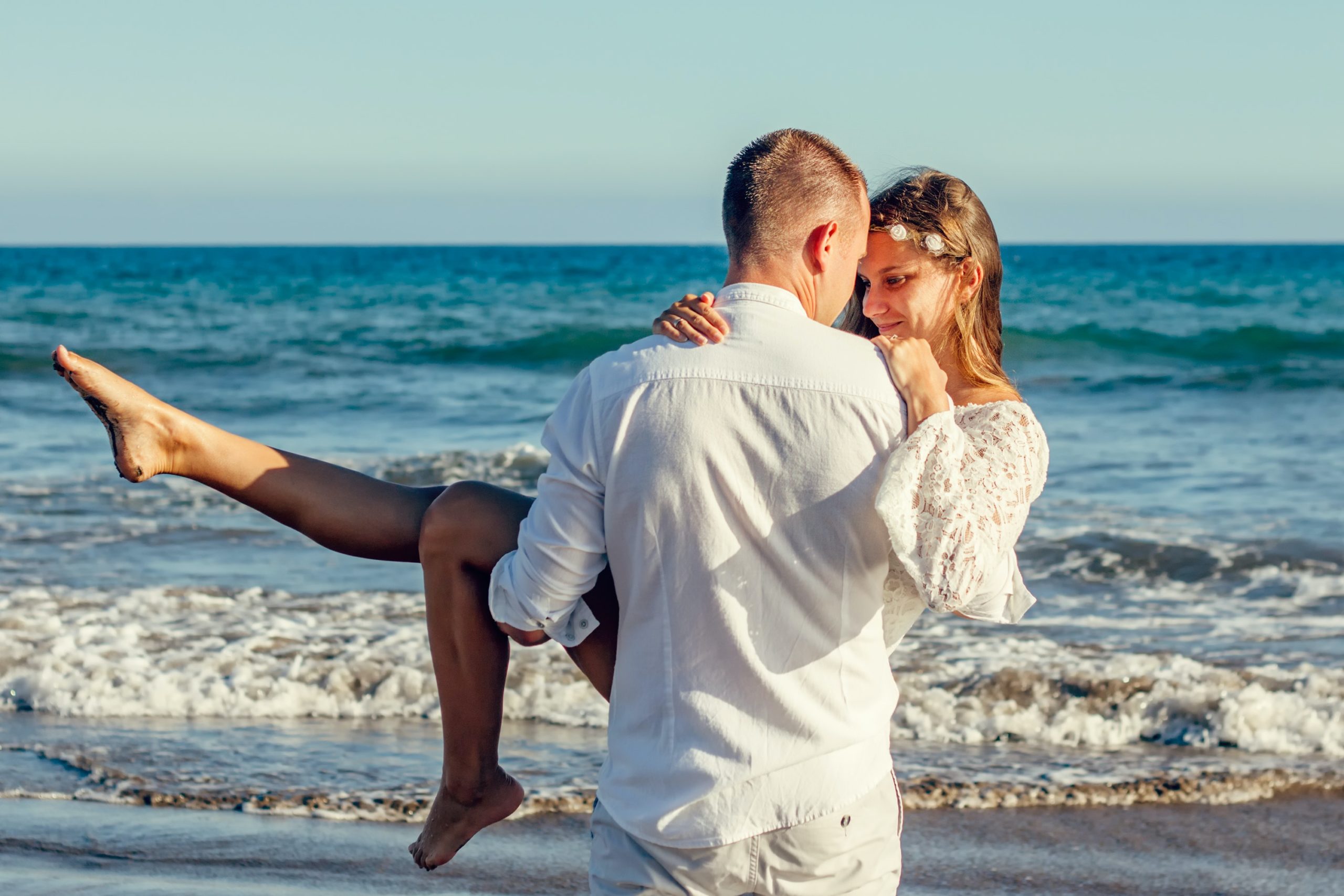 A man carrying his presumably wife on the beach.