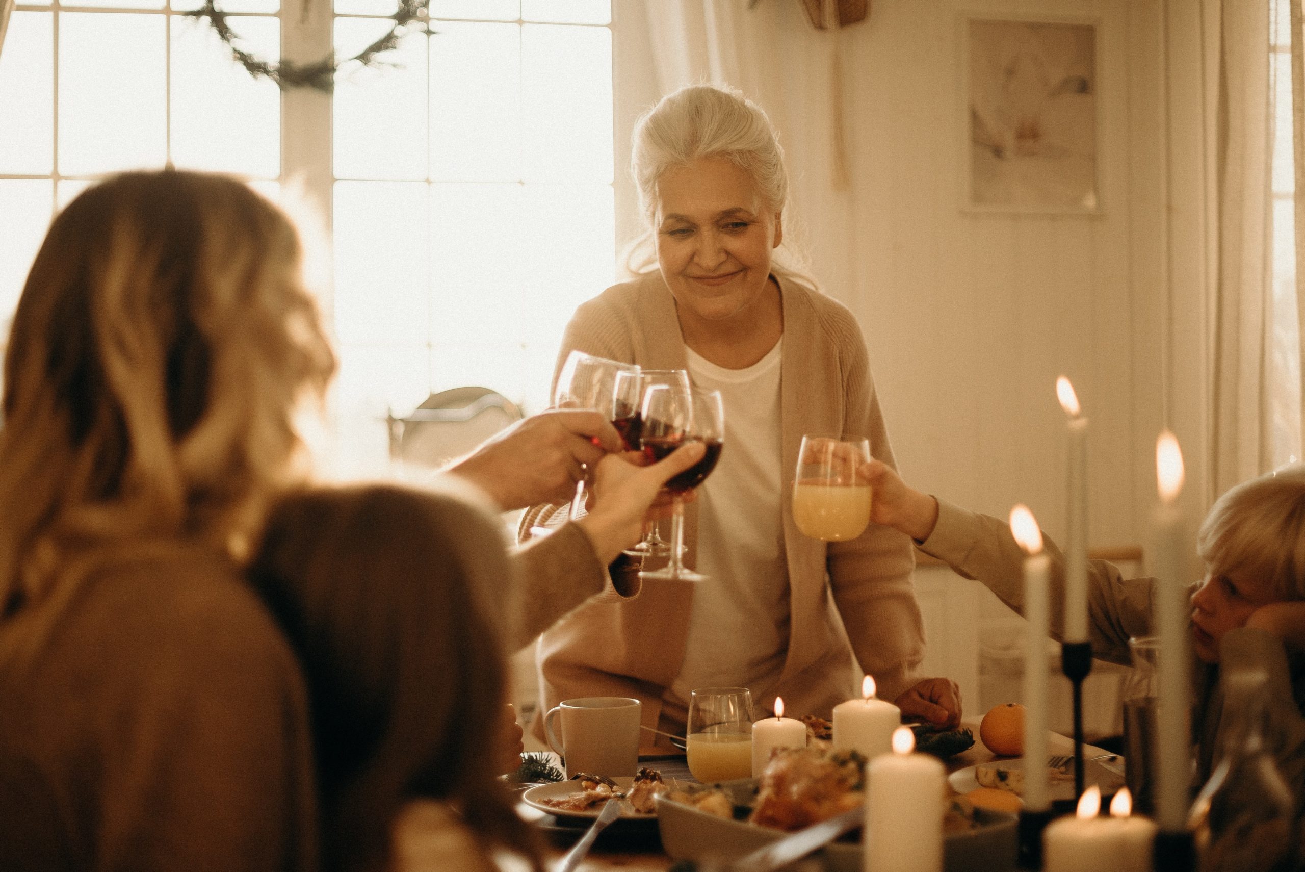 A woman standing to cheers her glass at a family dinner table.