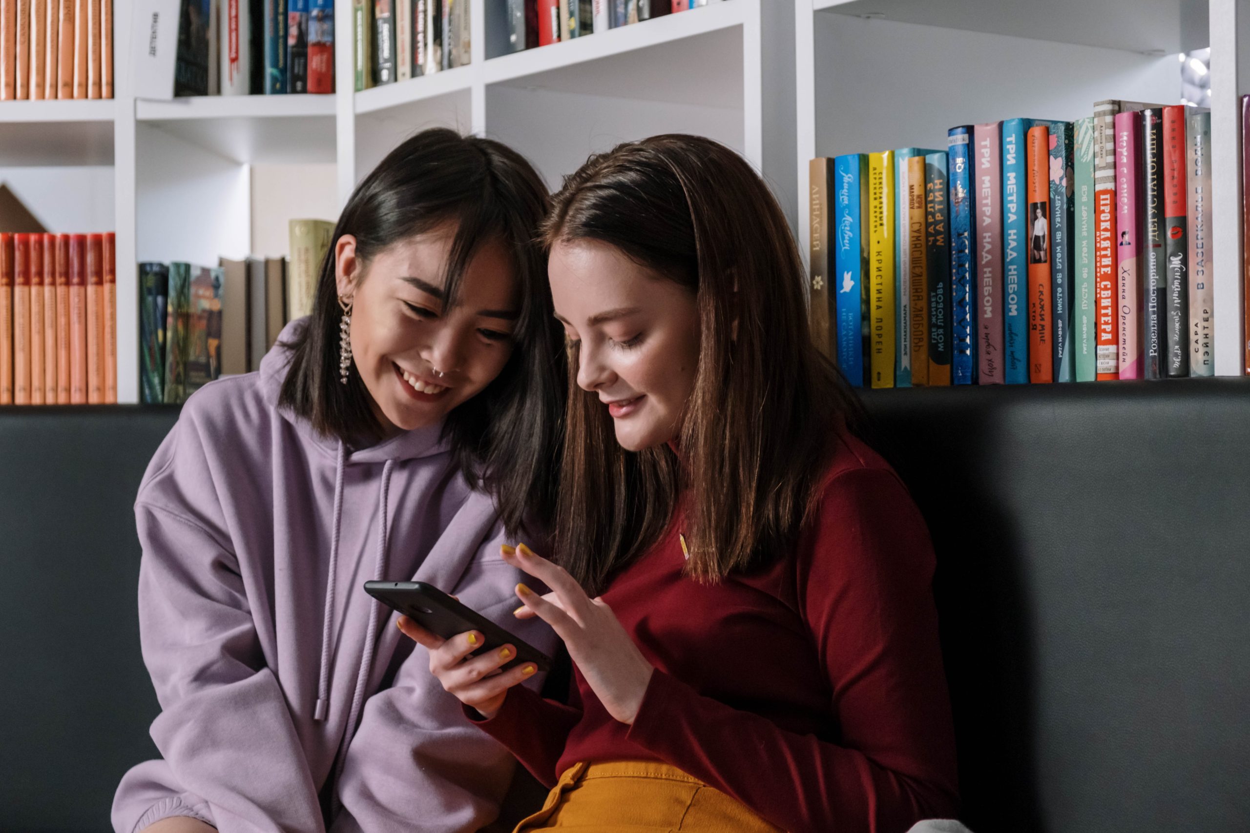 Two friends sitting next to each other, smiling, looking at one person's phone