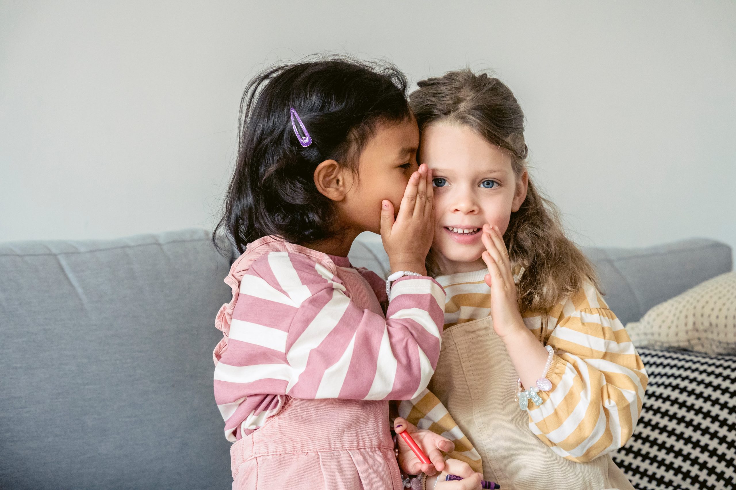 One little girl whispering into another's ear.