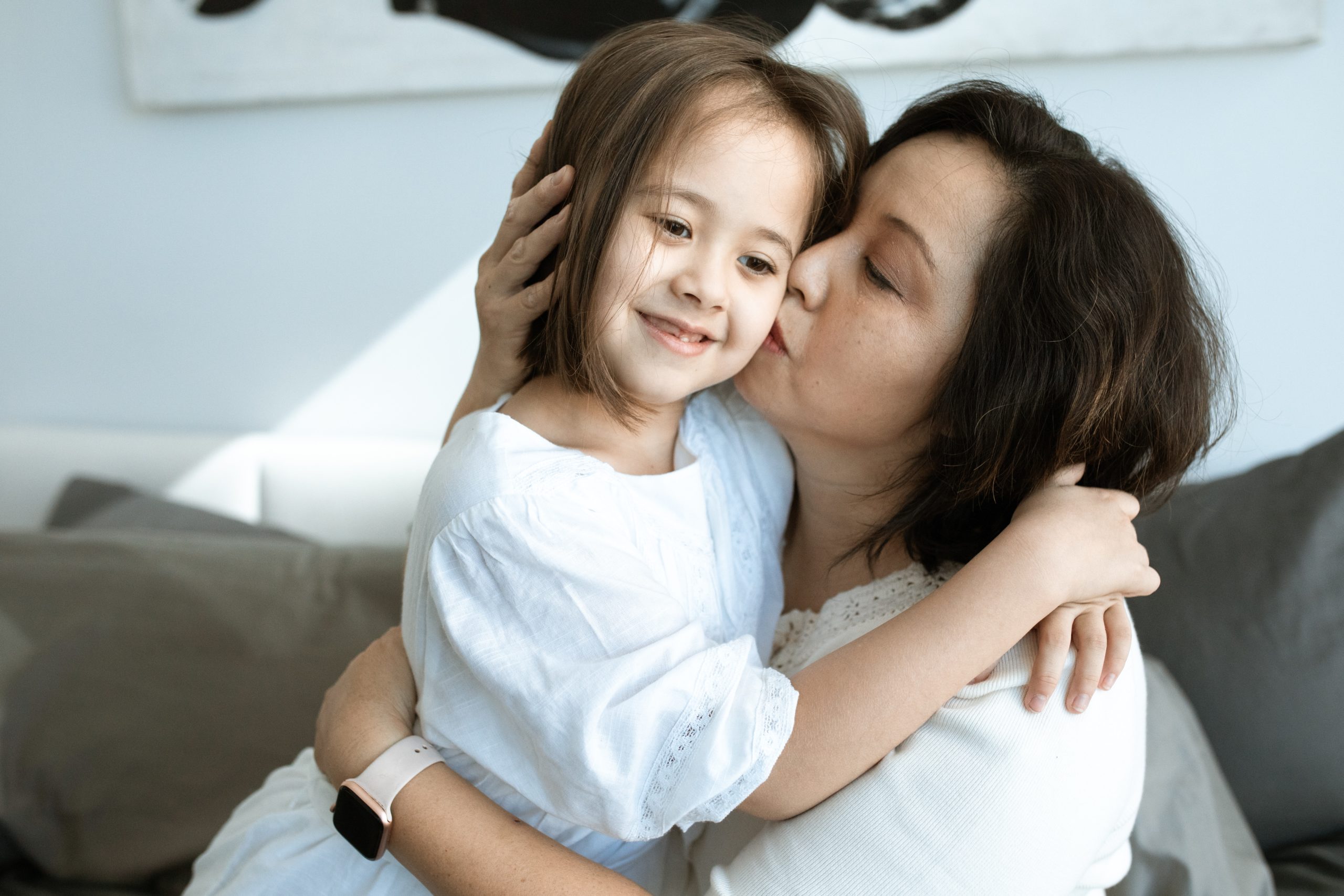 A woman embracing and kissing her young daughter on the cheek.
