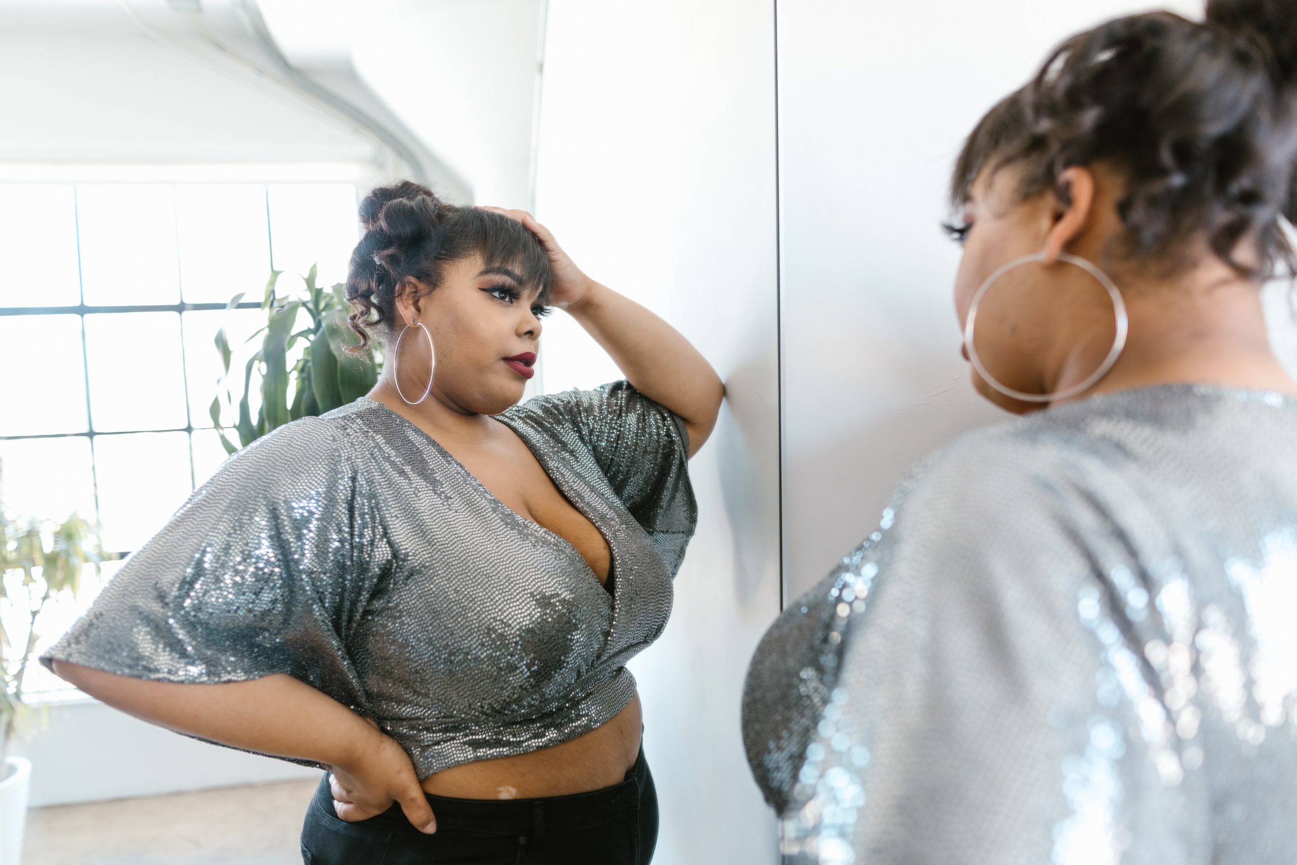 A woman in a sparkly silver crop top admiring herself in a mirror.
