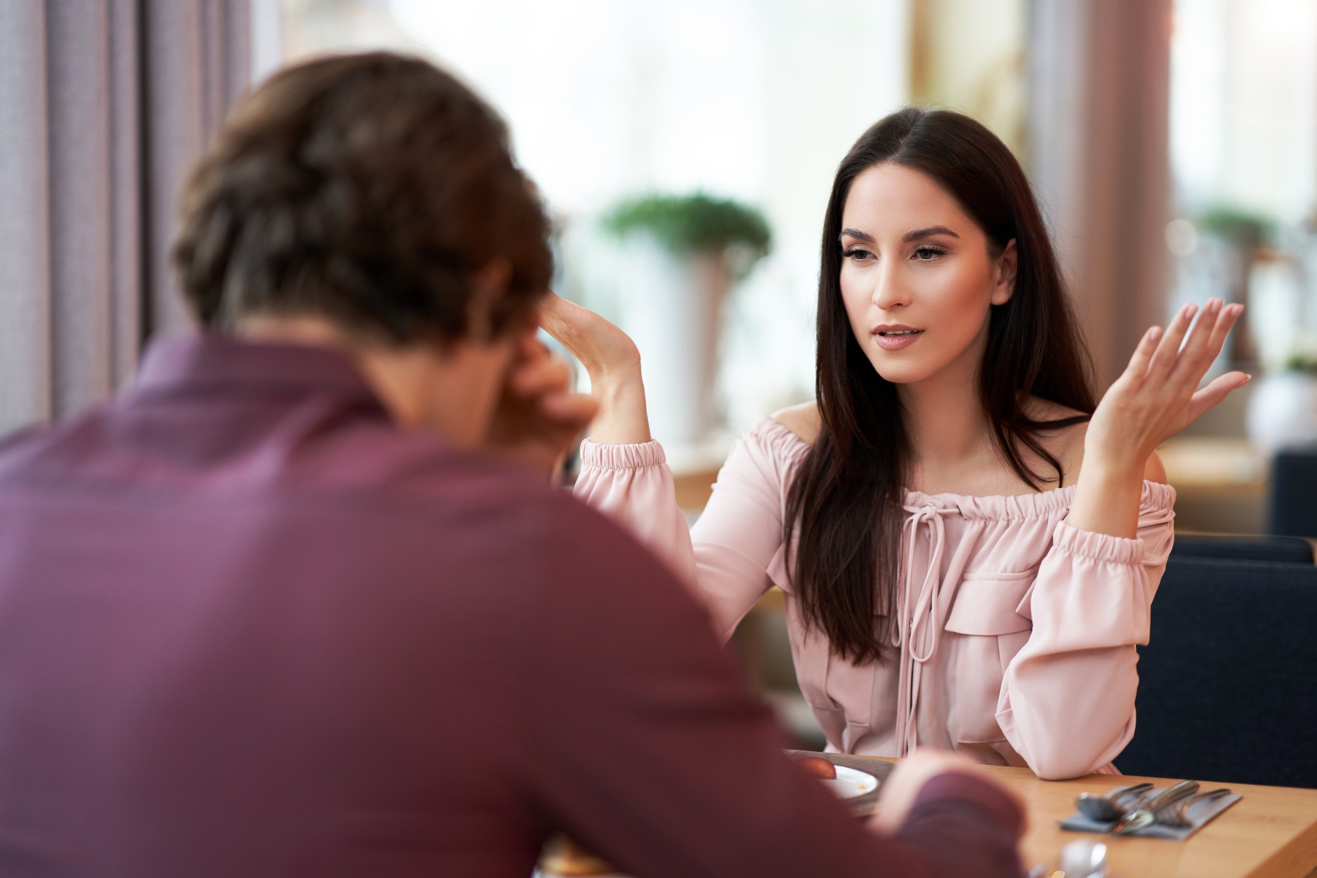 woman in pink looking frustrated hands raised at man with head down across table