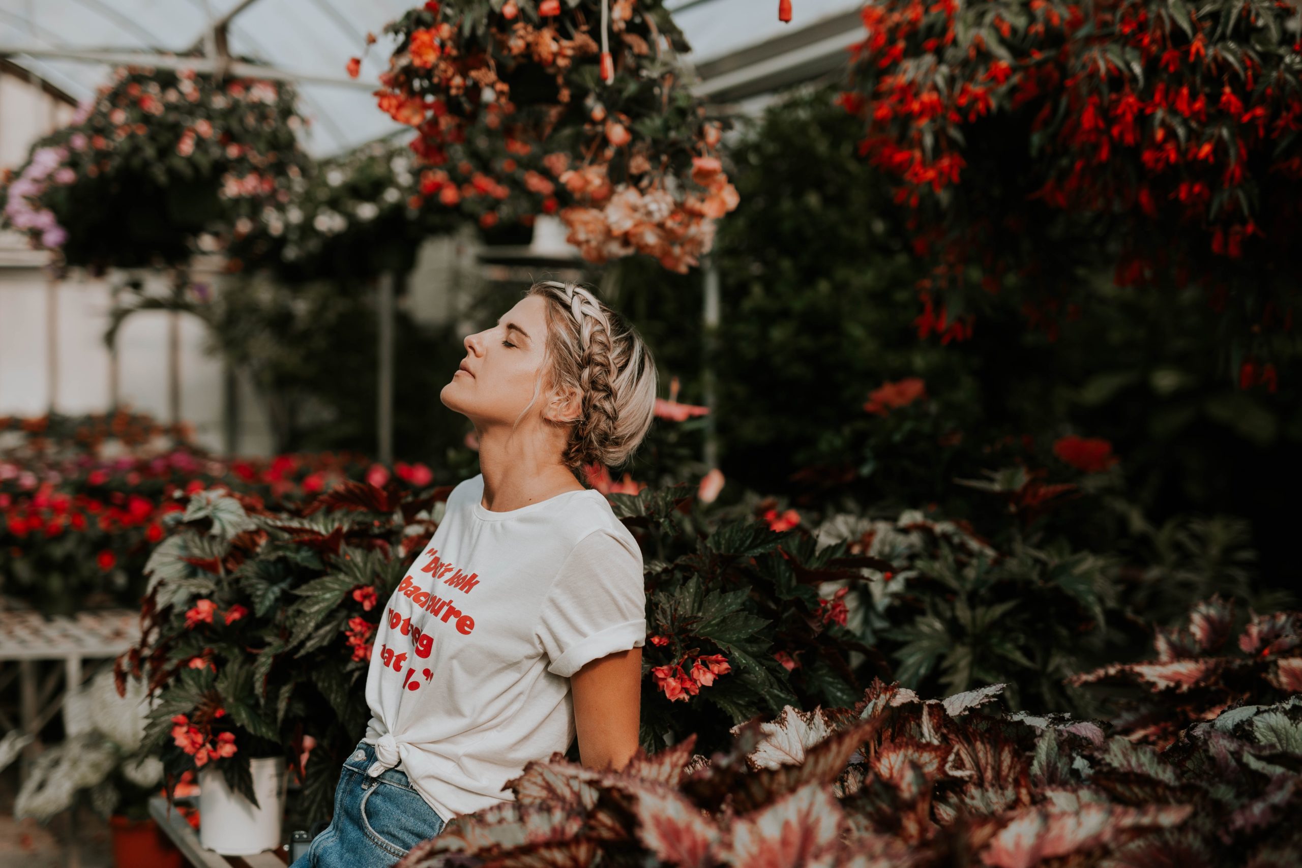 A woman standing among flowers, eyes closed, head tilted upwards.