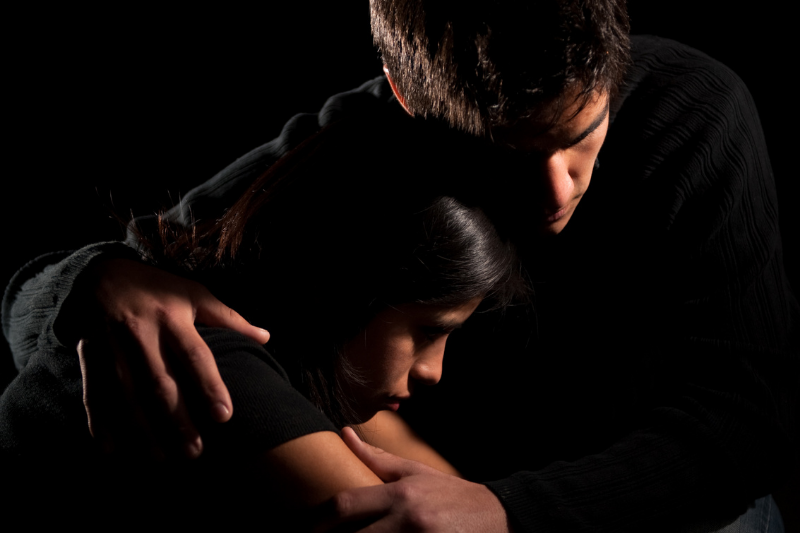 man hugs woman in dark lighting