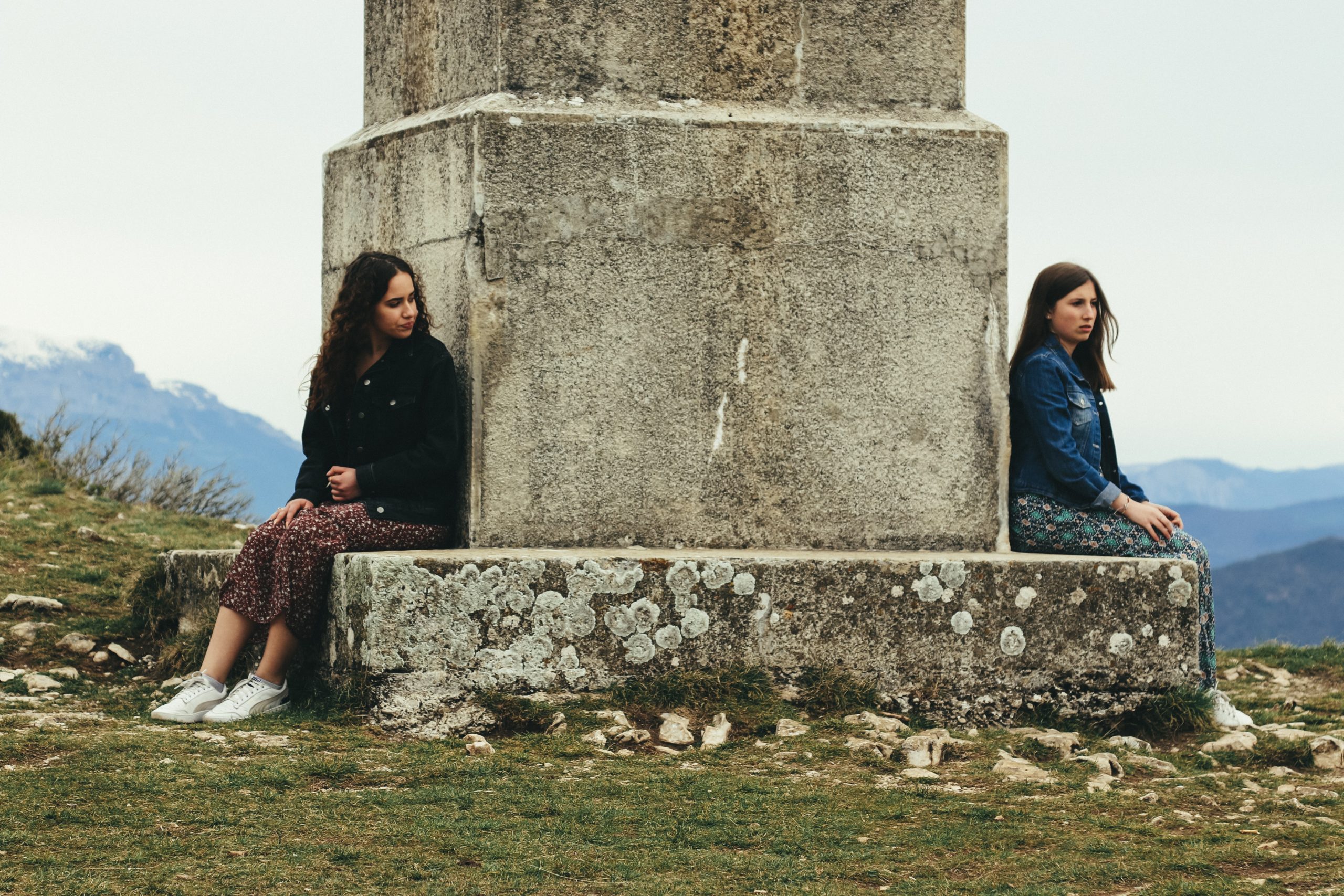 Two women sitting on opposite sides of a stone monument.