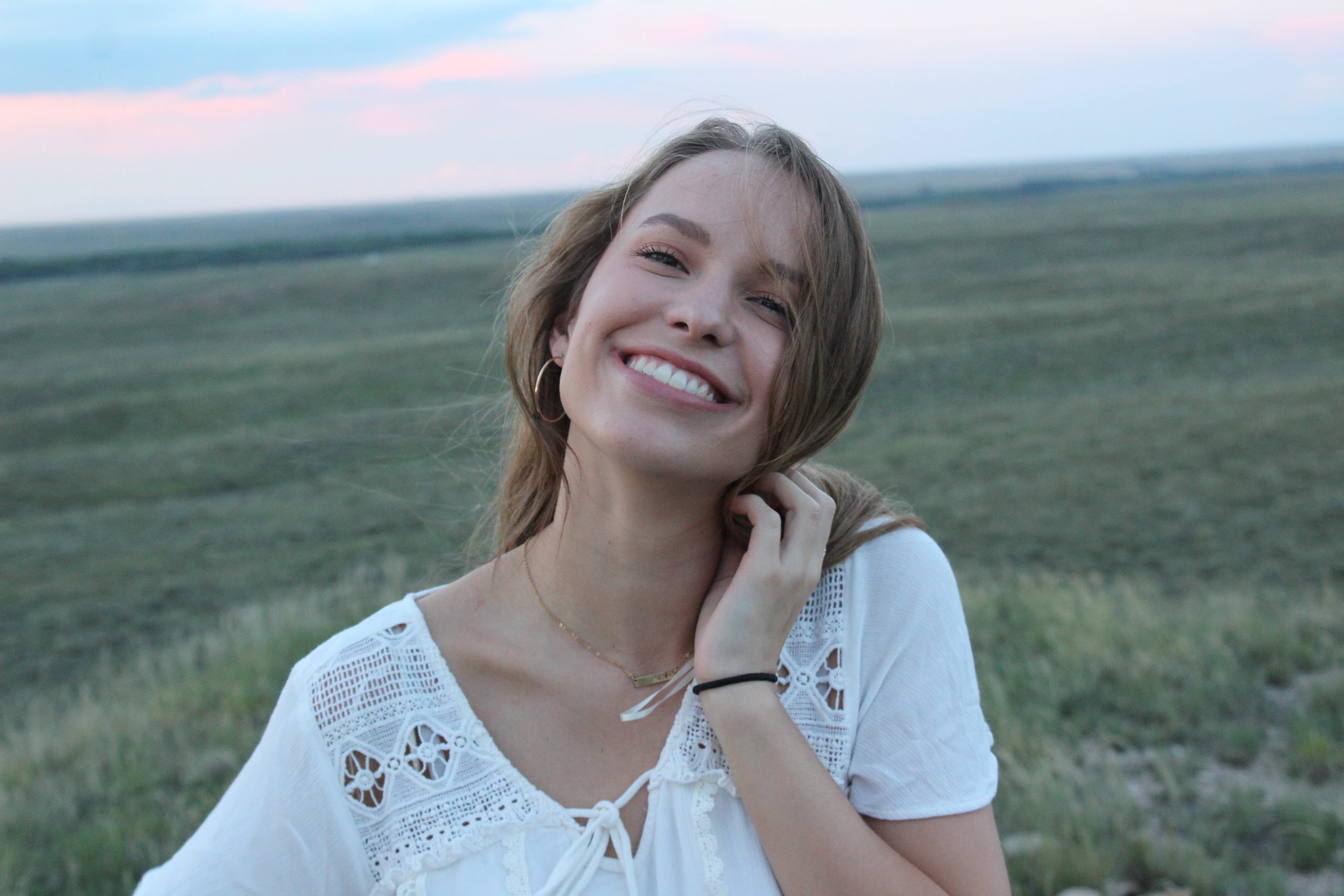 A woman smiling, standing in front of a field.