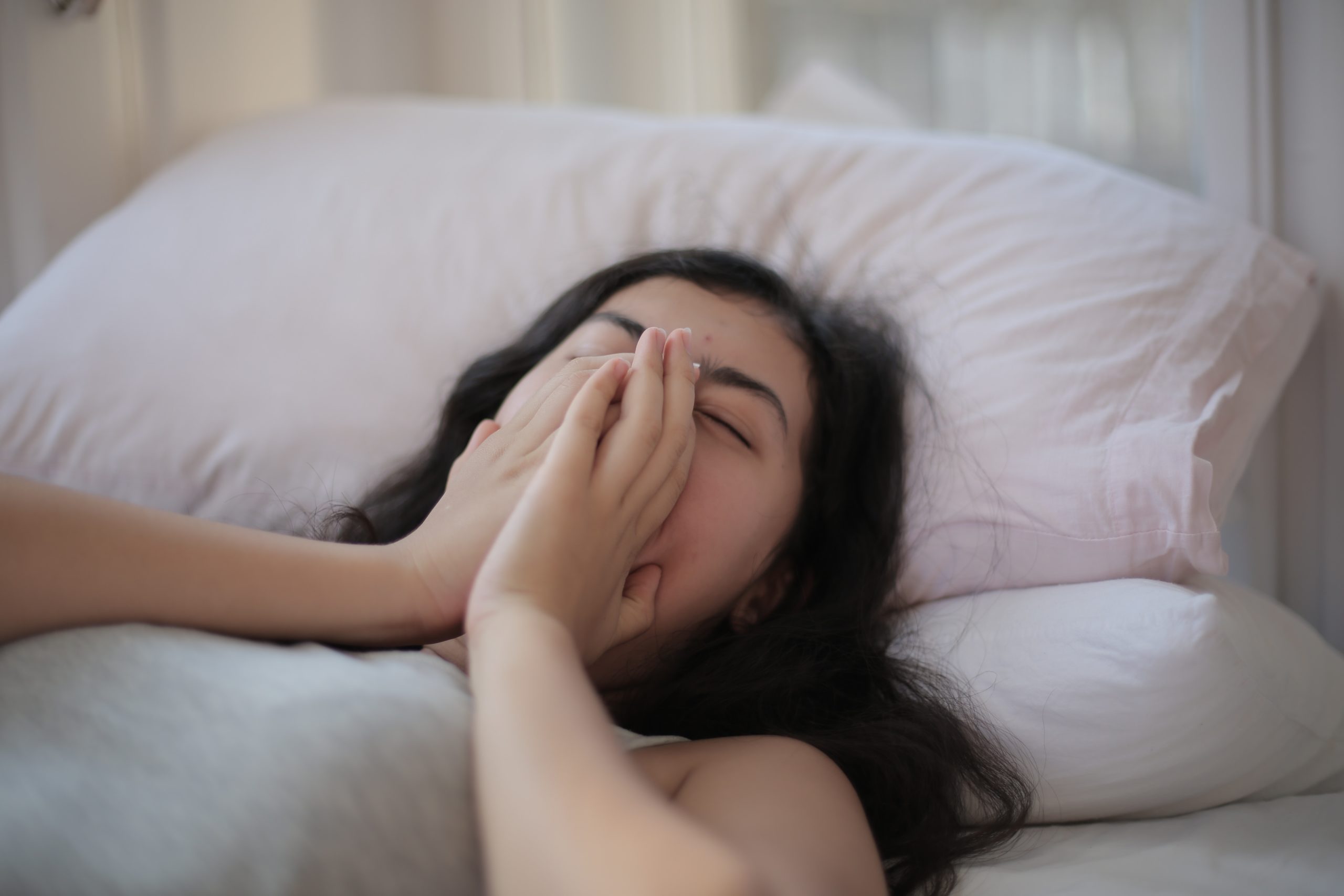 A girl asleep in bed, her hands covering her mouth.