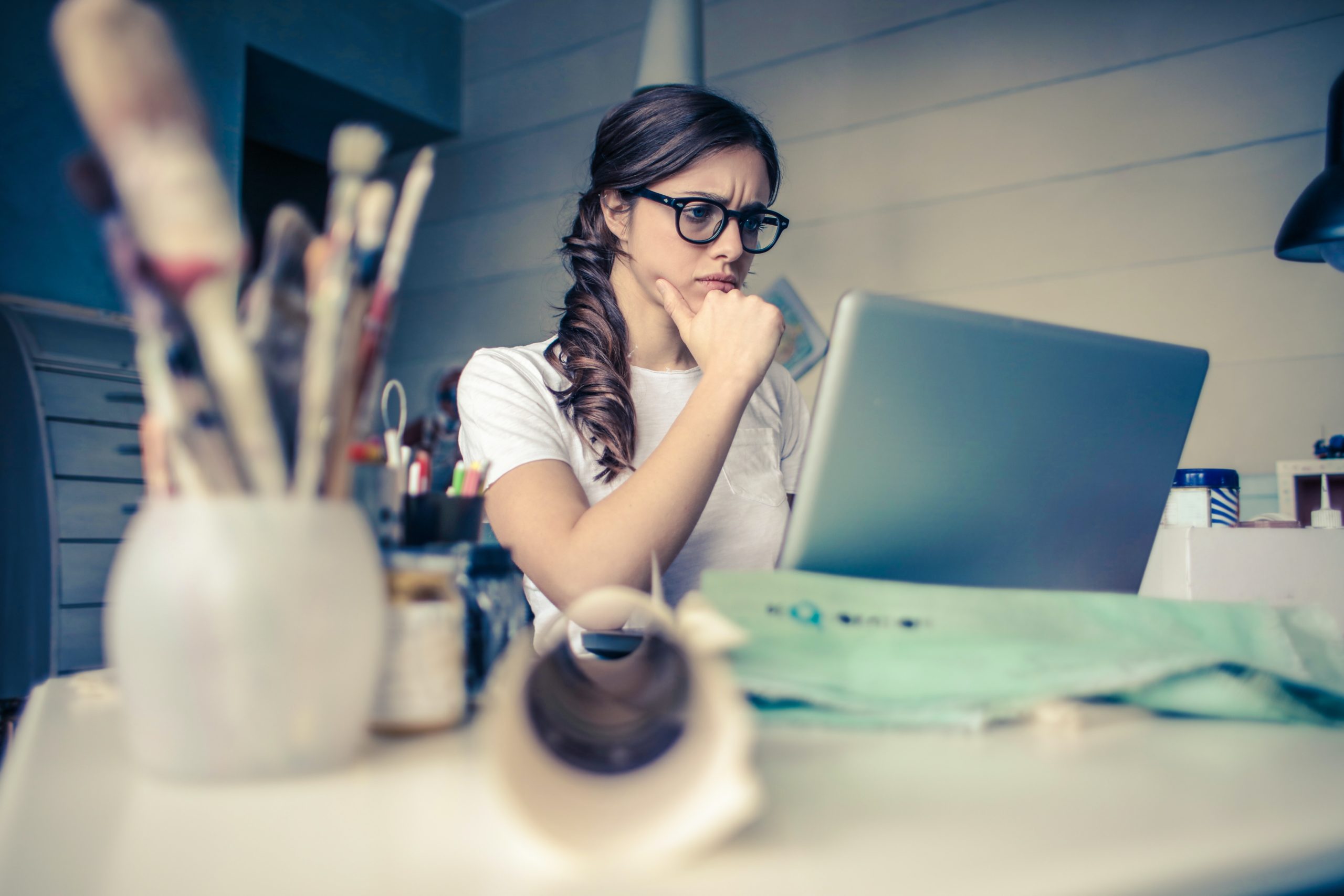 A woman seated at her desk, looking at her laptop with a focused expression.