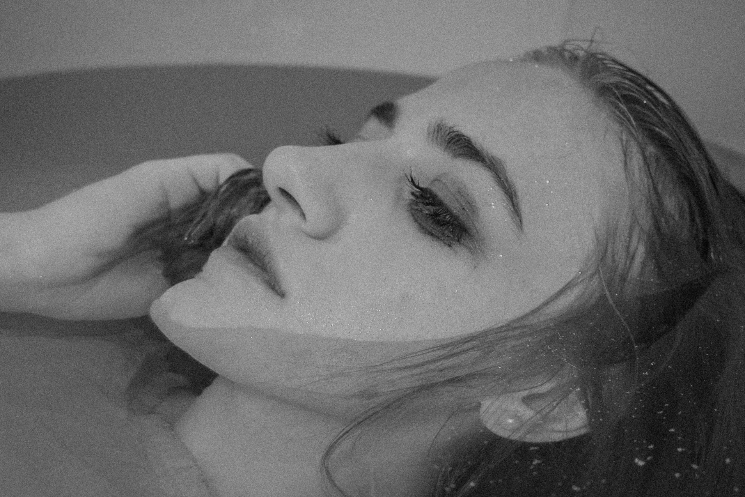 A grescale image of a woman's face half-submerged in a bathtub.