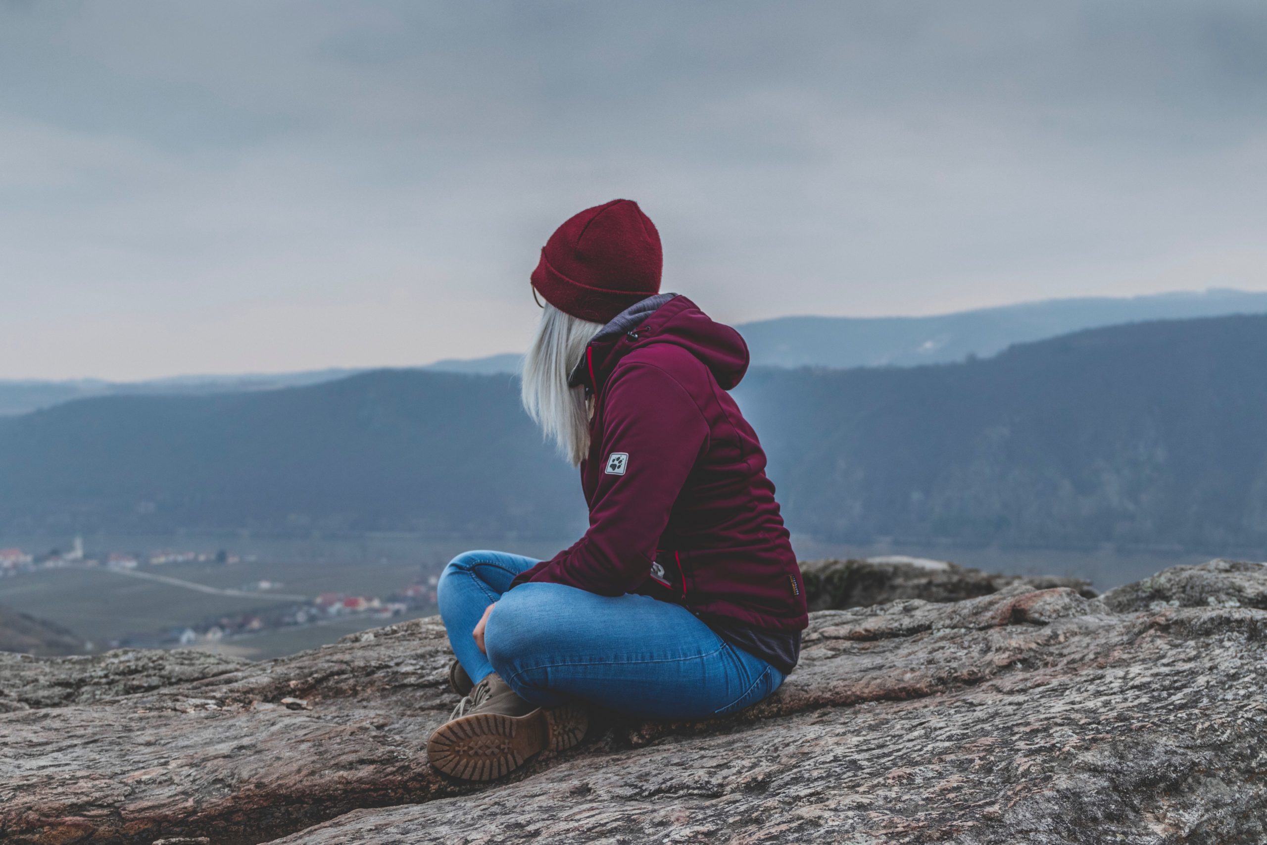 A woman sitting on the ground high above a field, looking away from the camera.