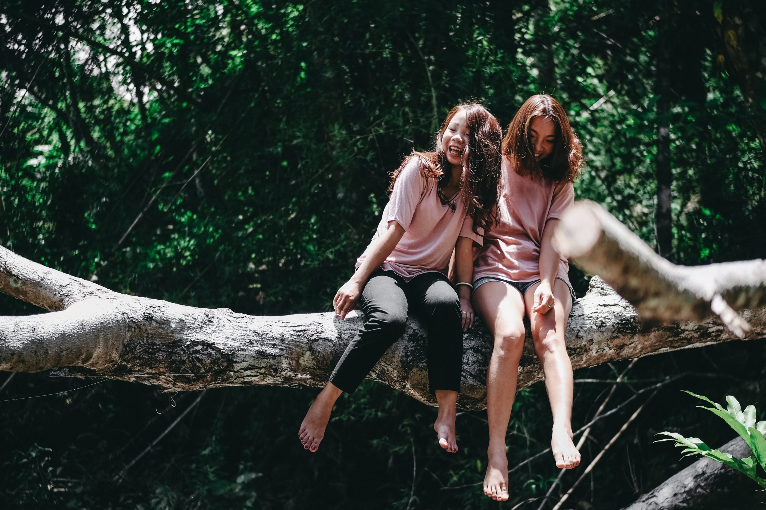 Two girls sitting on a log in the forest.