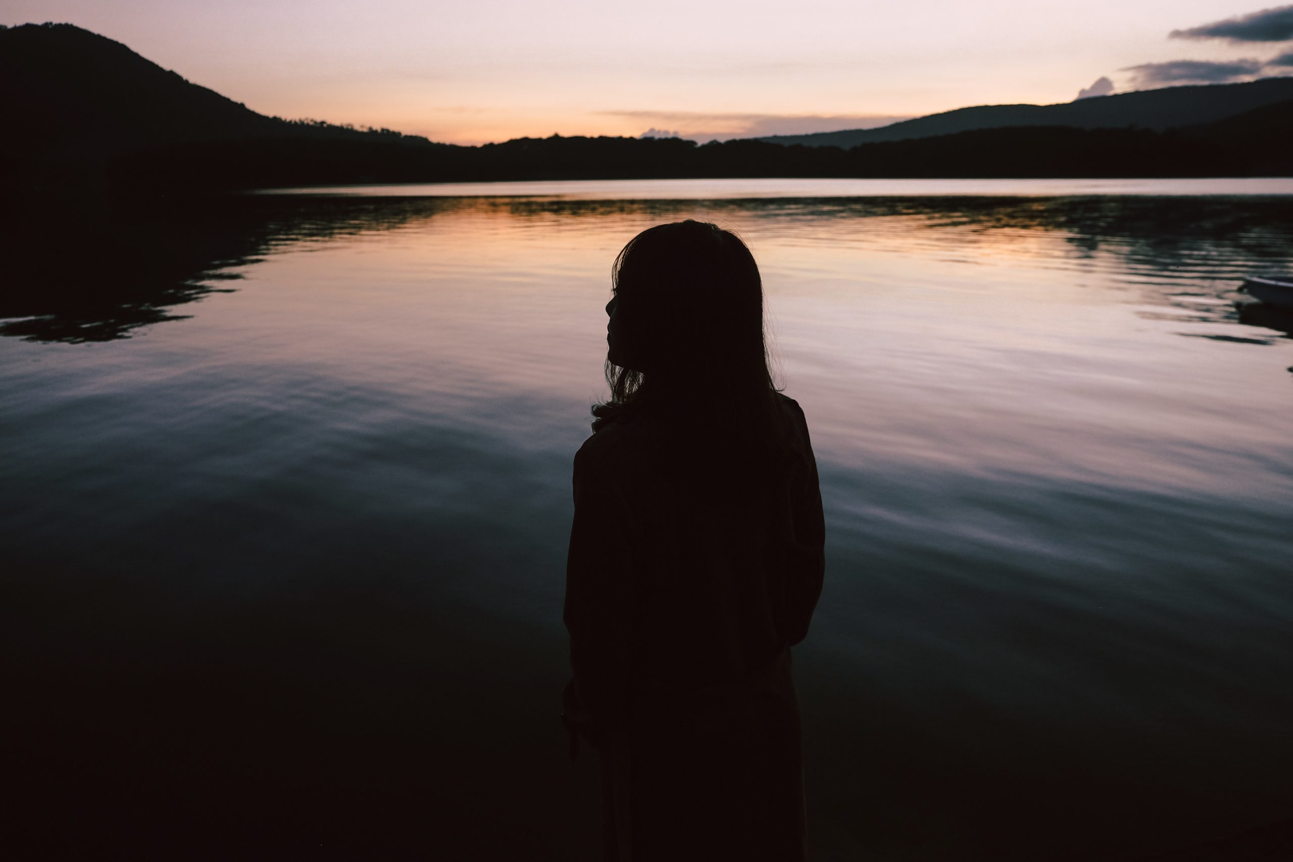 A silhouette of a woman standing in front of a lake.