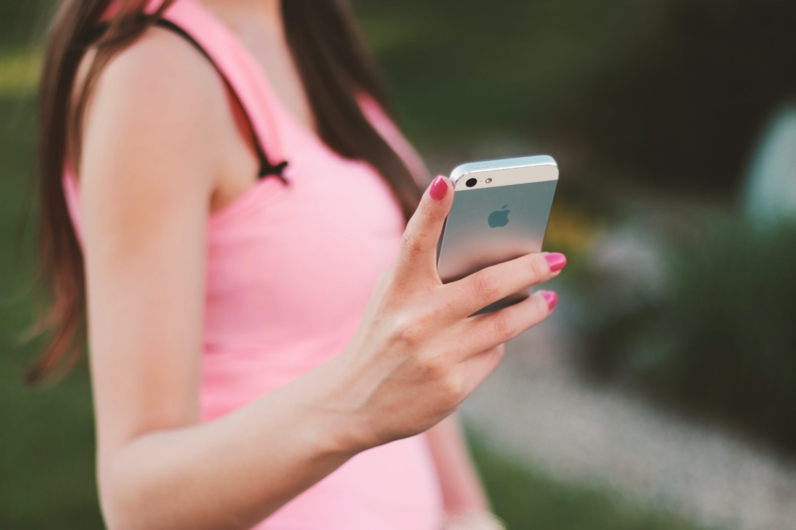 A woman in a pink shirt holding and looking at an iPhone.